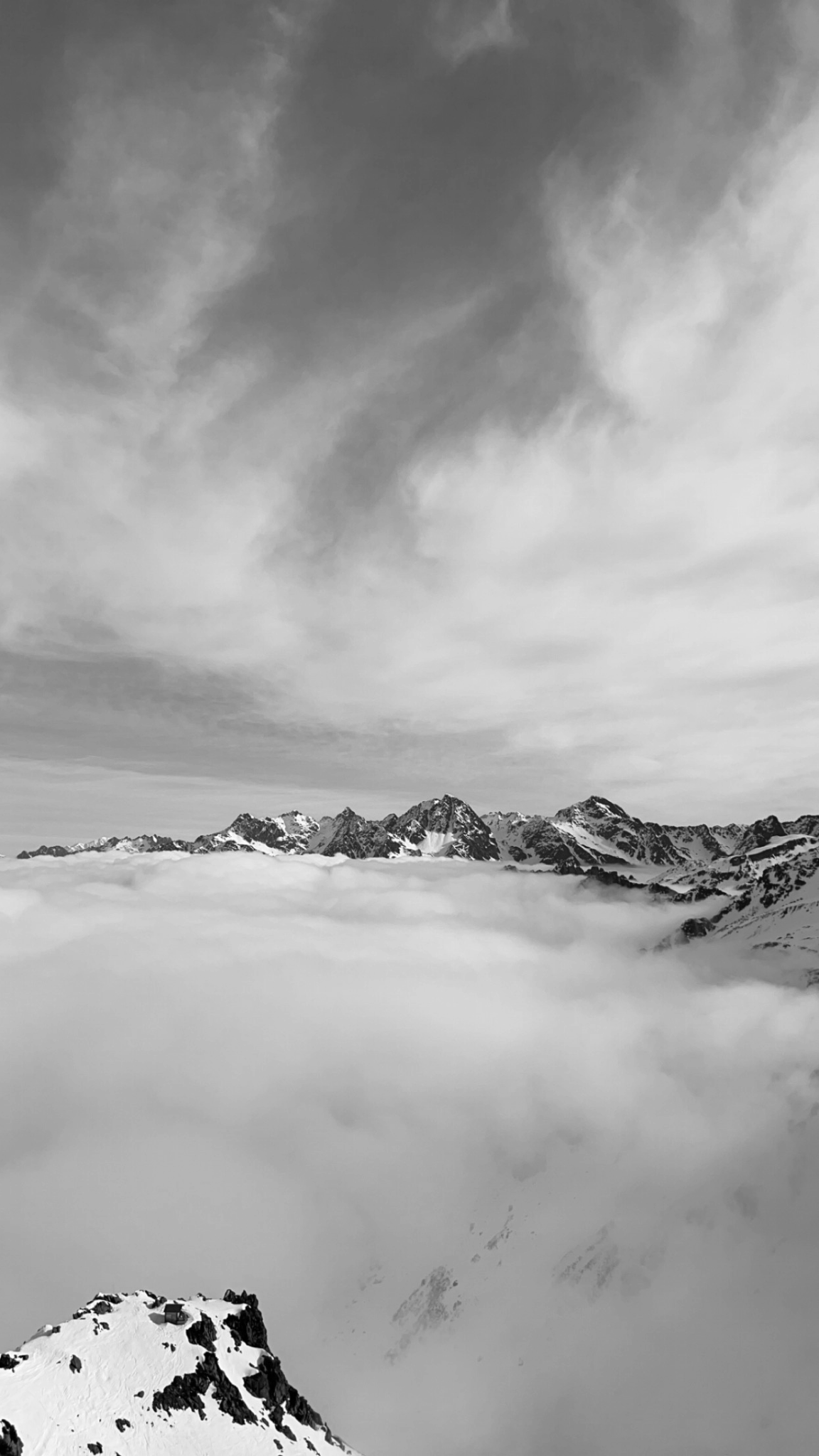 Chaîne de montagnes enneigées sous un ciel nuageux, vue en noir et blanc.