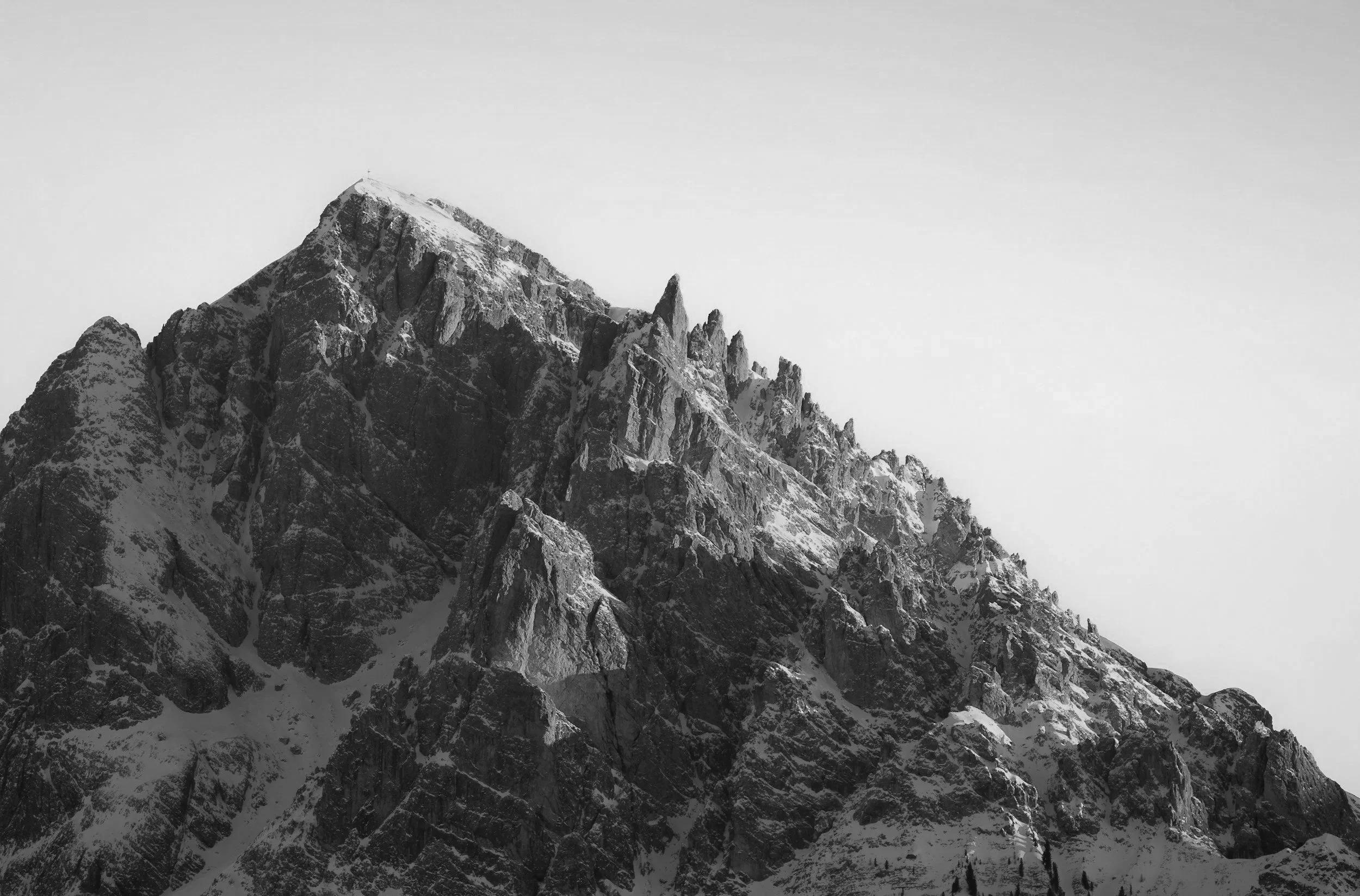 Montagne enneigée avec des sommets rocheux pointus sous un ciel nuageux.