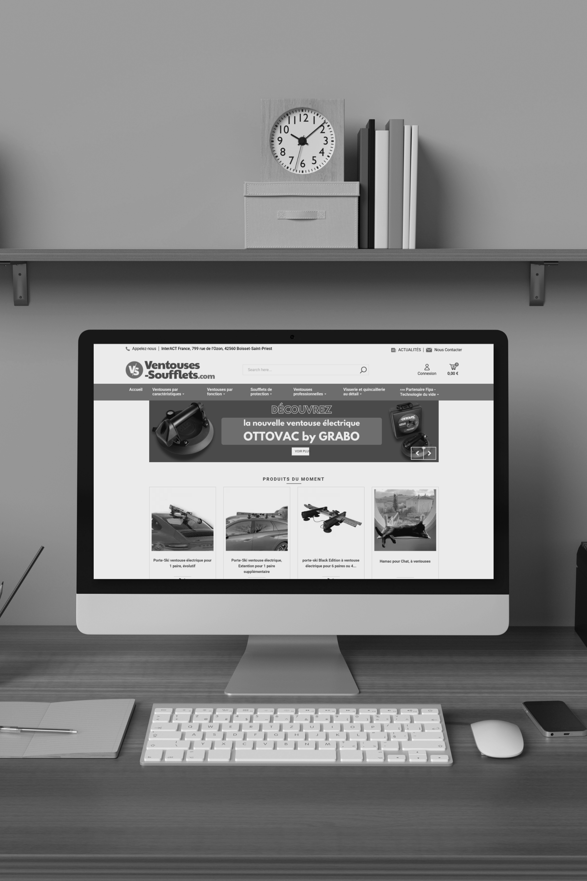 Un bureau avec un ordinateur affichant un site web en français, une souris, un clavier, un carnet de notes avec un stylo, et une horloge murale dans une pièce moderne.