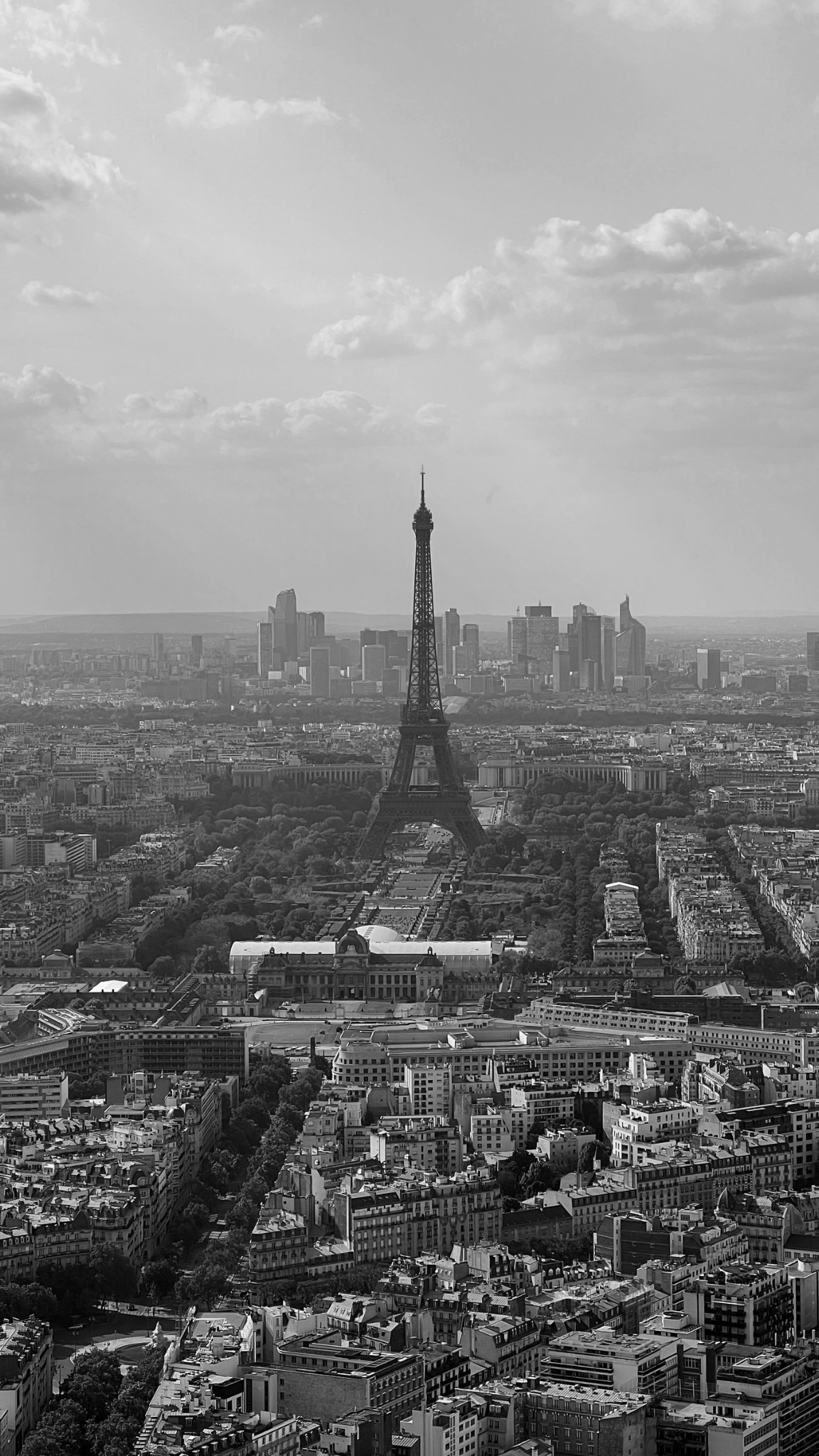 Vue de Paris avec la Tour Eiffel au centre, entourée de bâtiments urbains et un ciel partiellement nuageux.