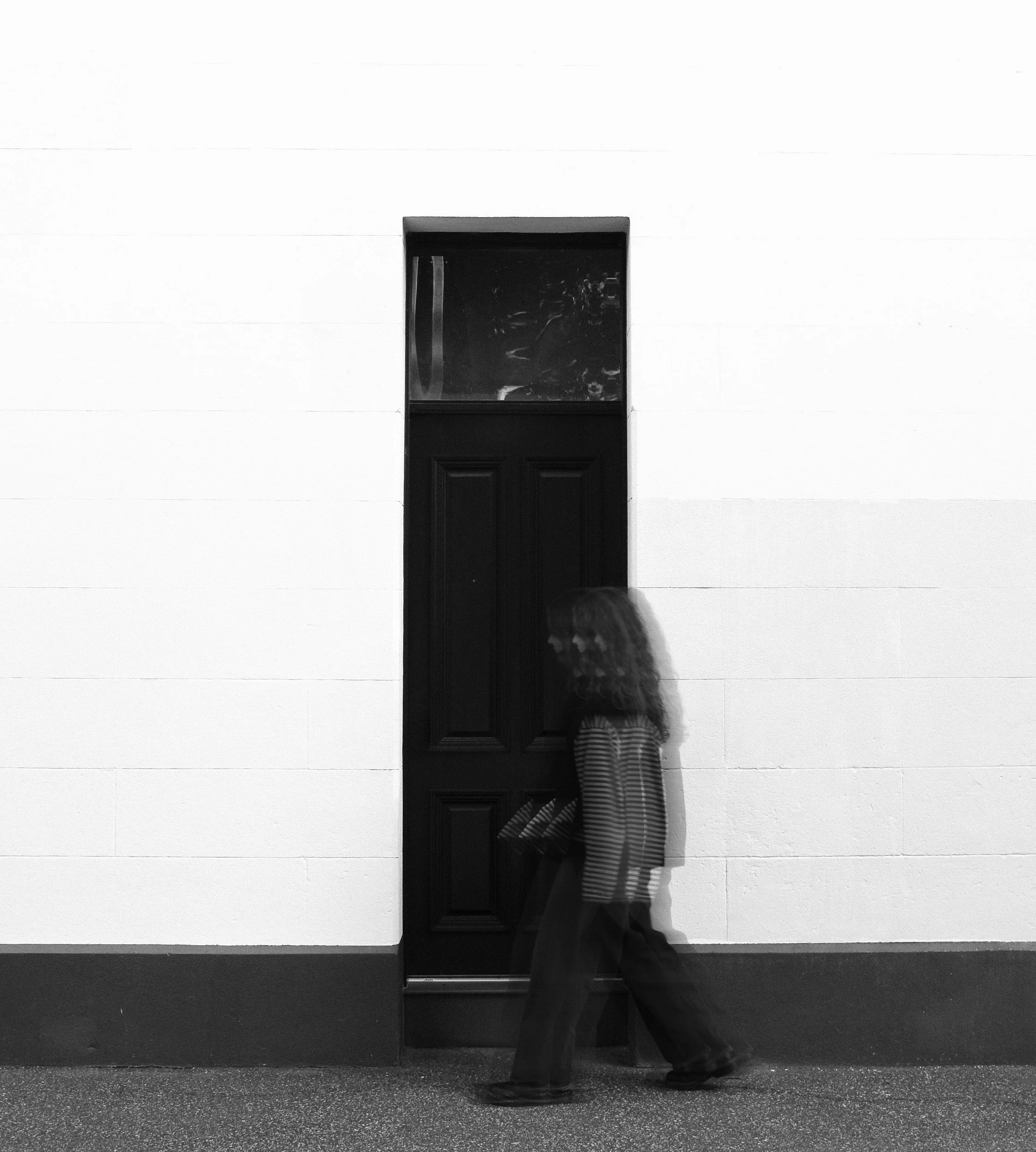 A person wearing a striped dress walking past a mirror with a black frame in front of white wall panels.