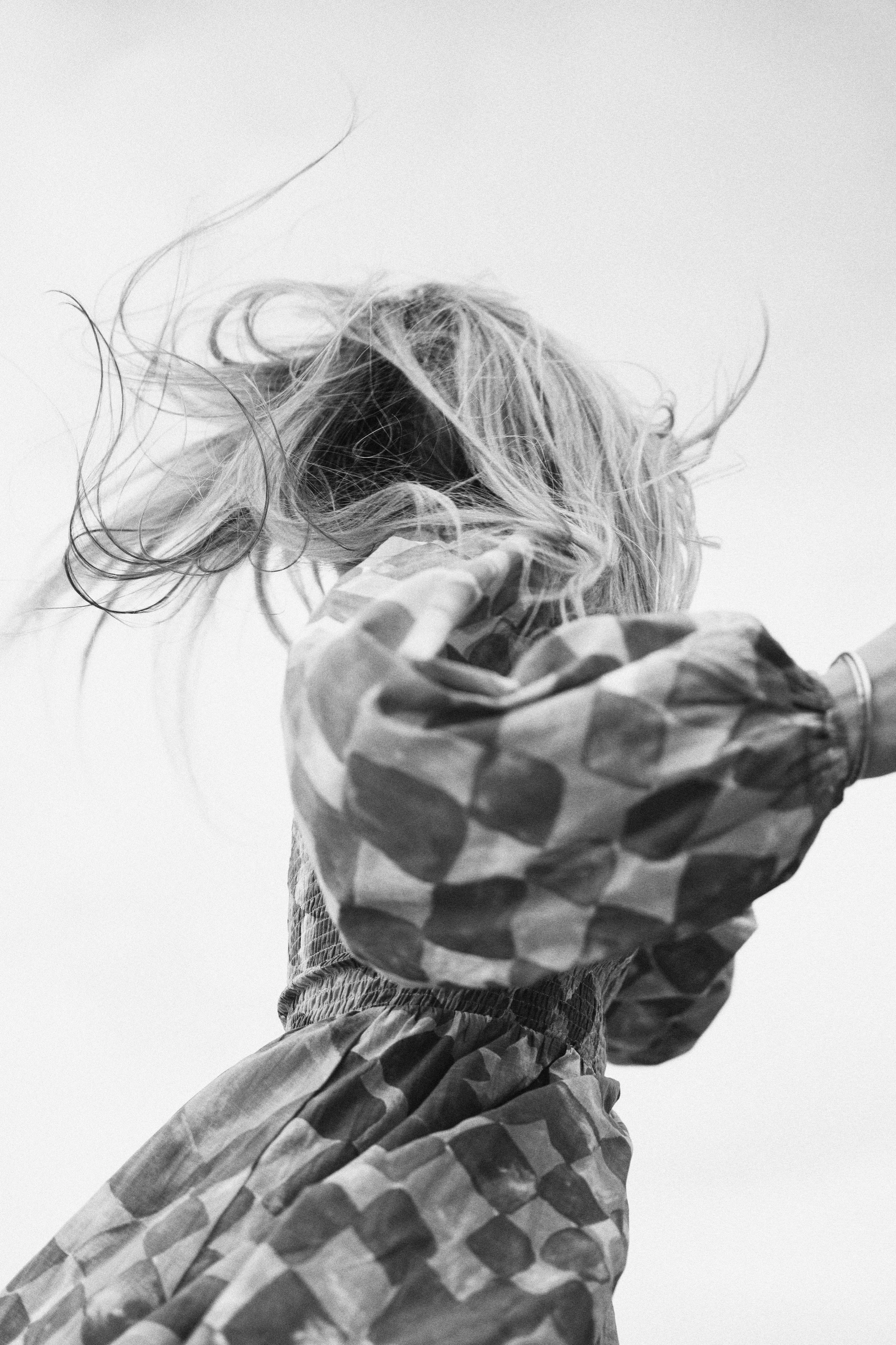 Brand campaign shoot for Melbourne small business  A black and white photo of a person with wavy hair, wearing a checkered jacket and matching checkered pants, seen from the back, against a plain light background.