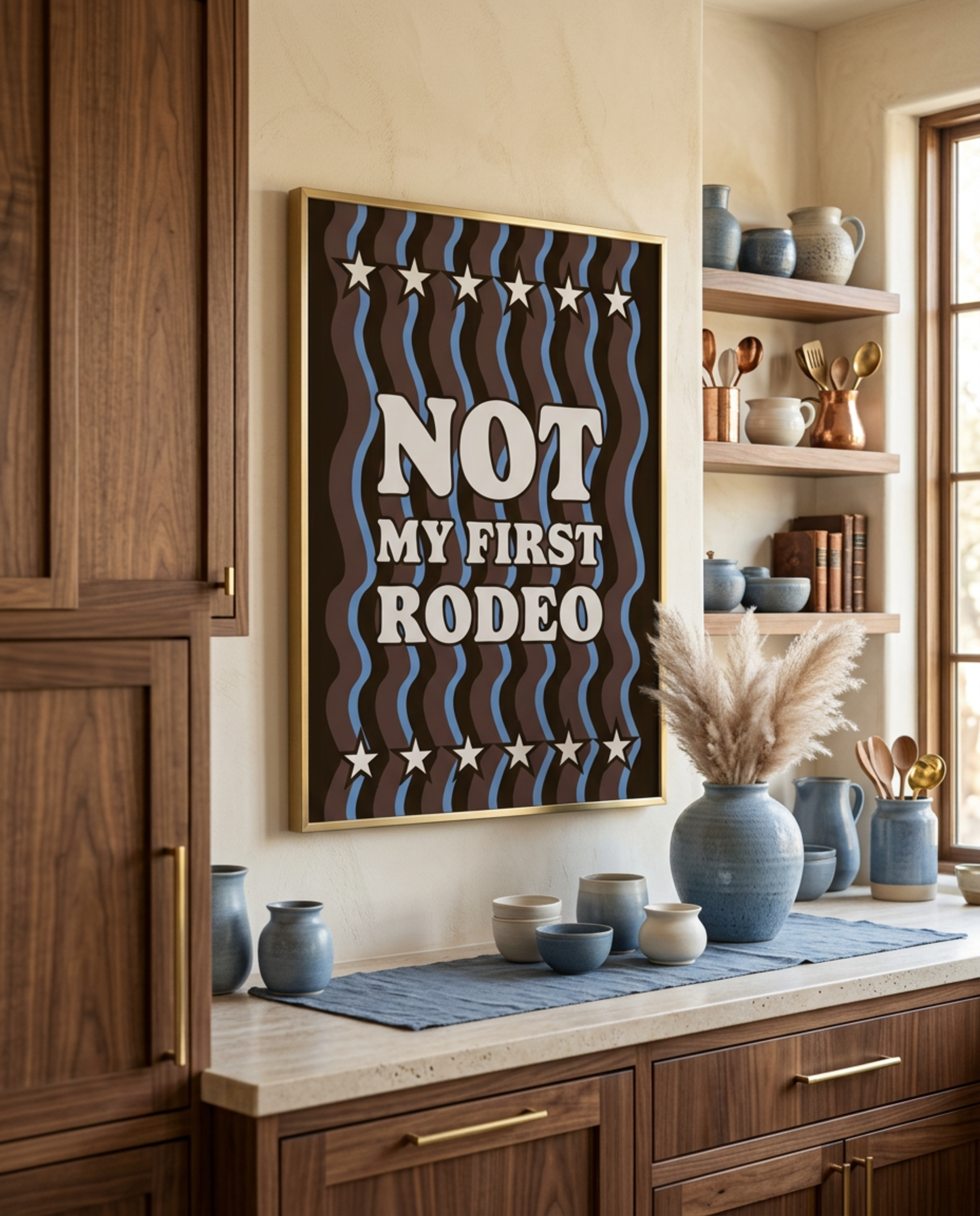 Not My First Rodeo typography print in brown and blue, framed in a walnut kitchen with blue pottery