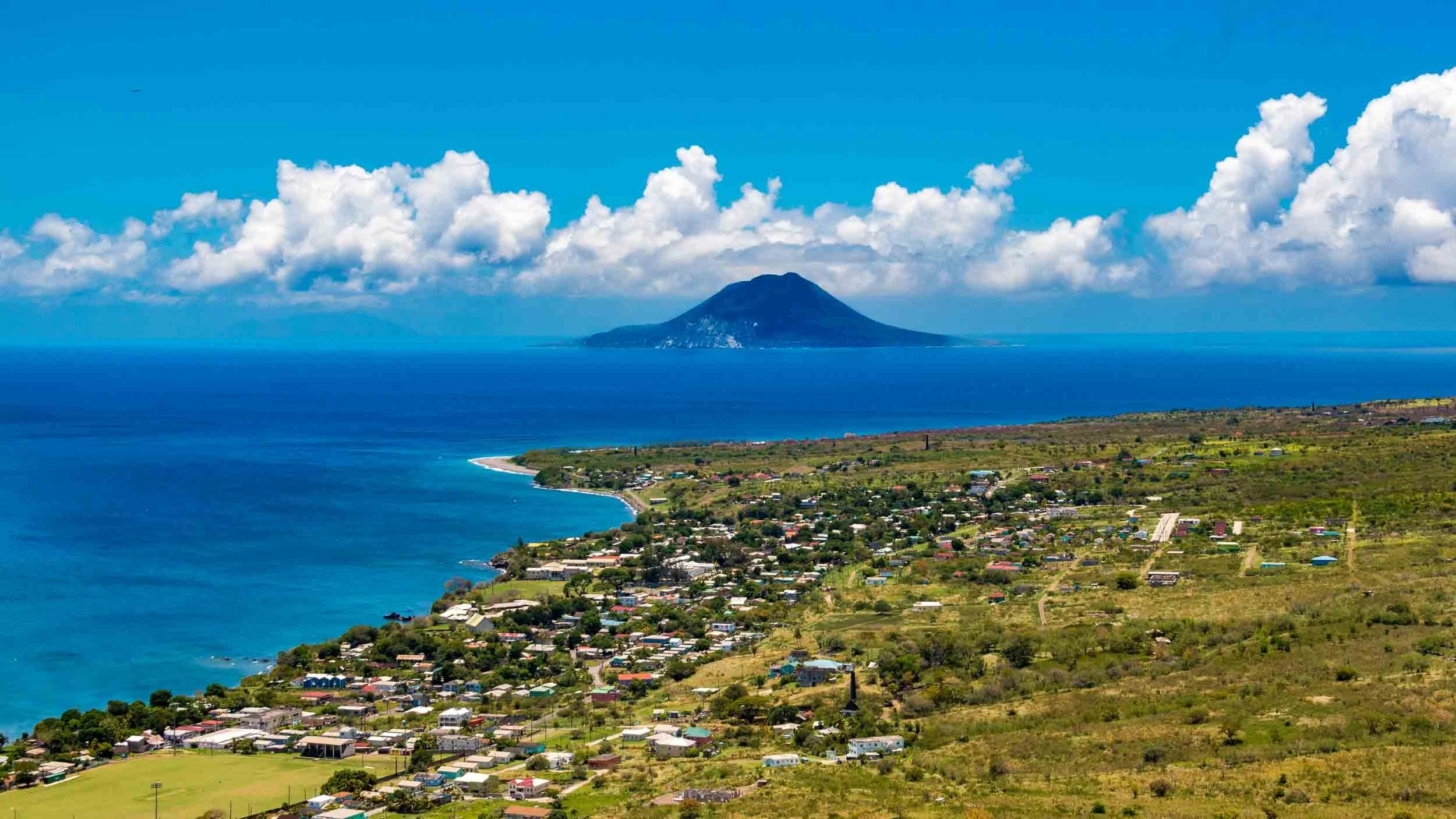 The island is Sint Eustatius (known as Statia). The peak is the volcanic cone of The Quill, a dormant stratovolcano. The residential area is Sandy Point Town. The photo was taken from Brimstone Hill Fortress National Park. May 5, 2017.
