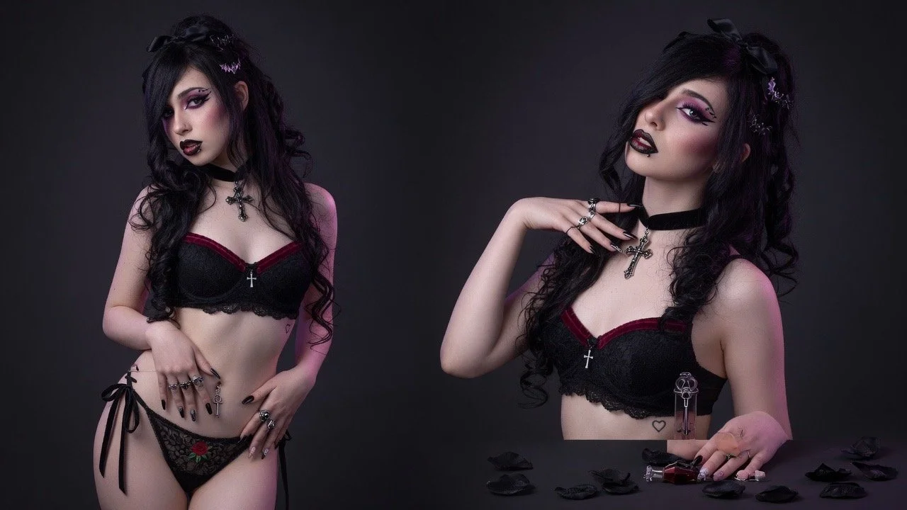 Young woman with black hair and gothic style makeup poses in black lingerie with red accents, jewelry, and accessories against a dark background.