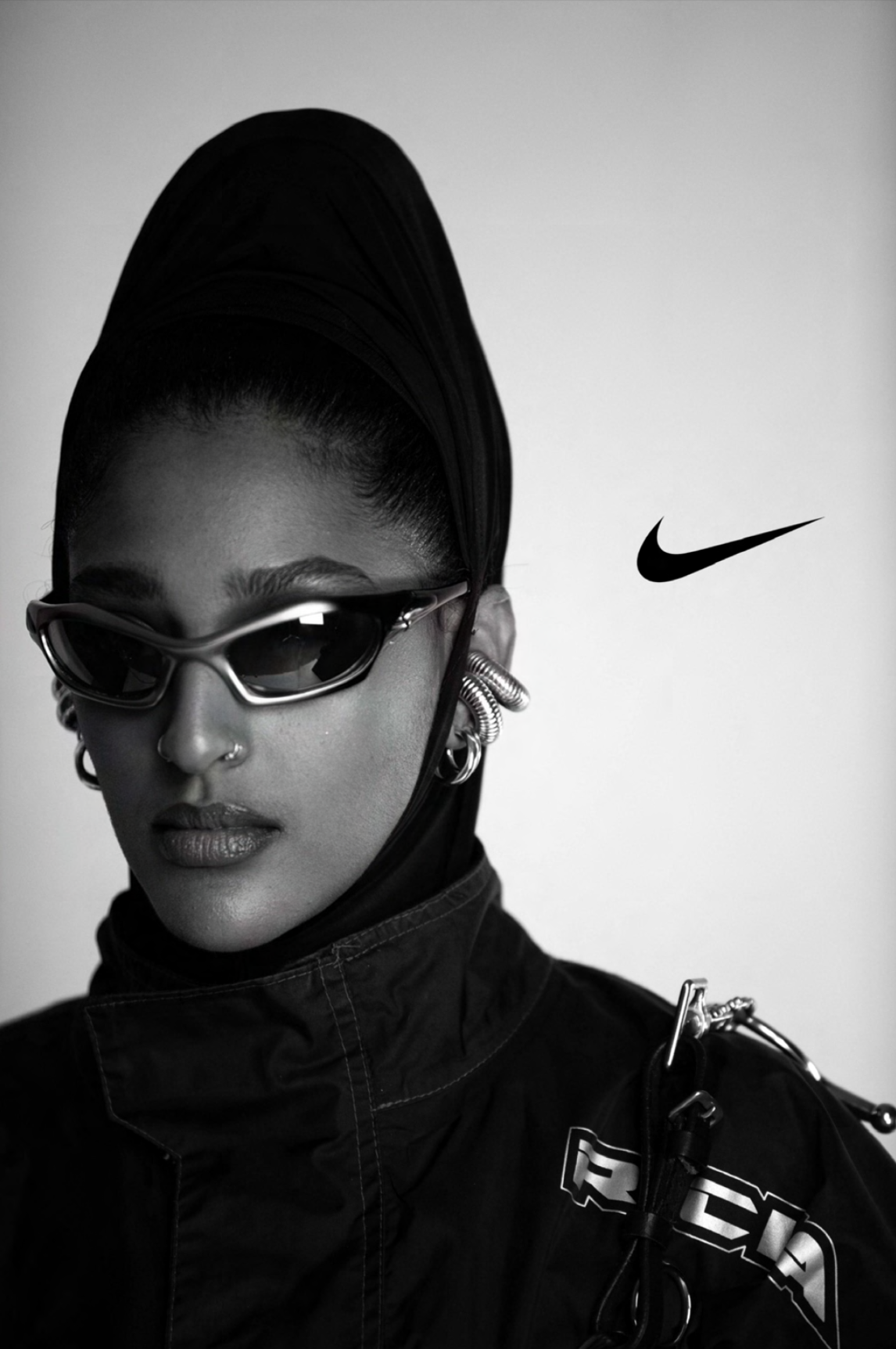 Stylish woman wearing sunglasses, large hoop earrings, a nose ring, and a black headscarf, with a Nike logo in the background.