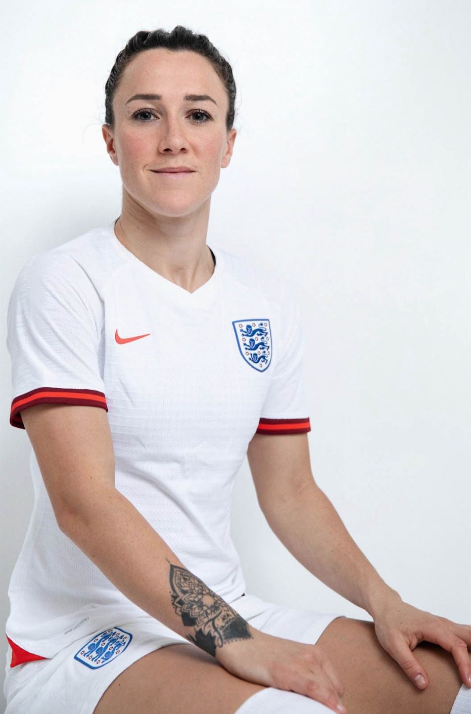 A female soccer player wearing a white England national team jersey with the Three Lions crest and Nike logo, sitting against a plain background.