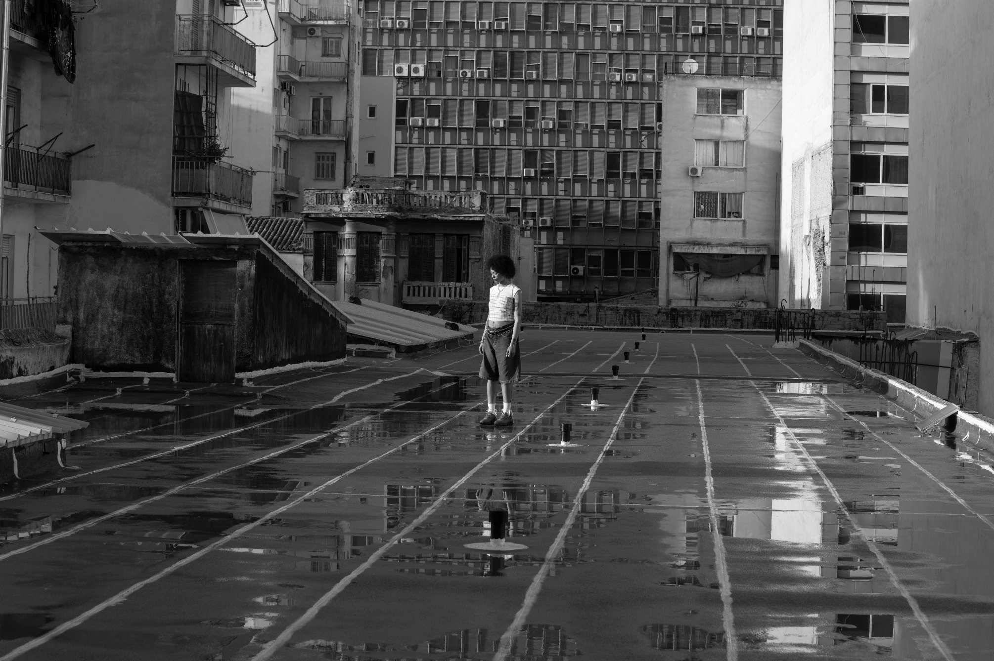 A person standing on a wet rooftop in a city with buildings in the background, black and white photograph.
