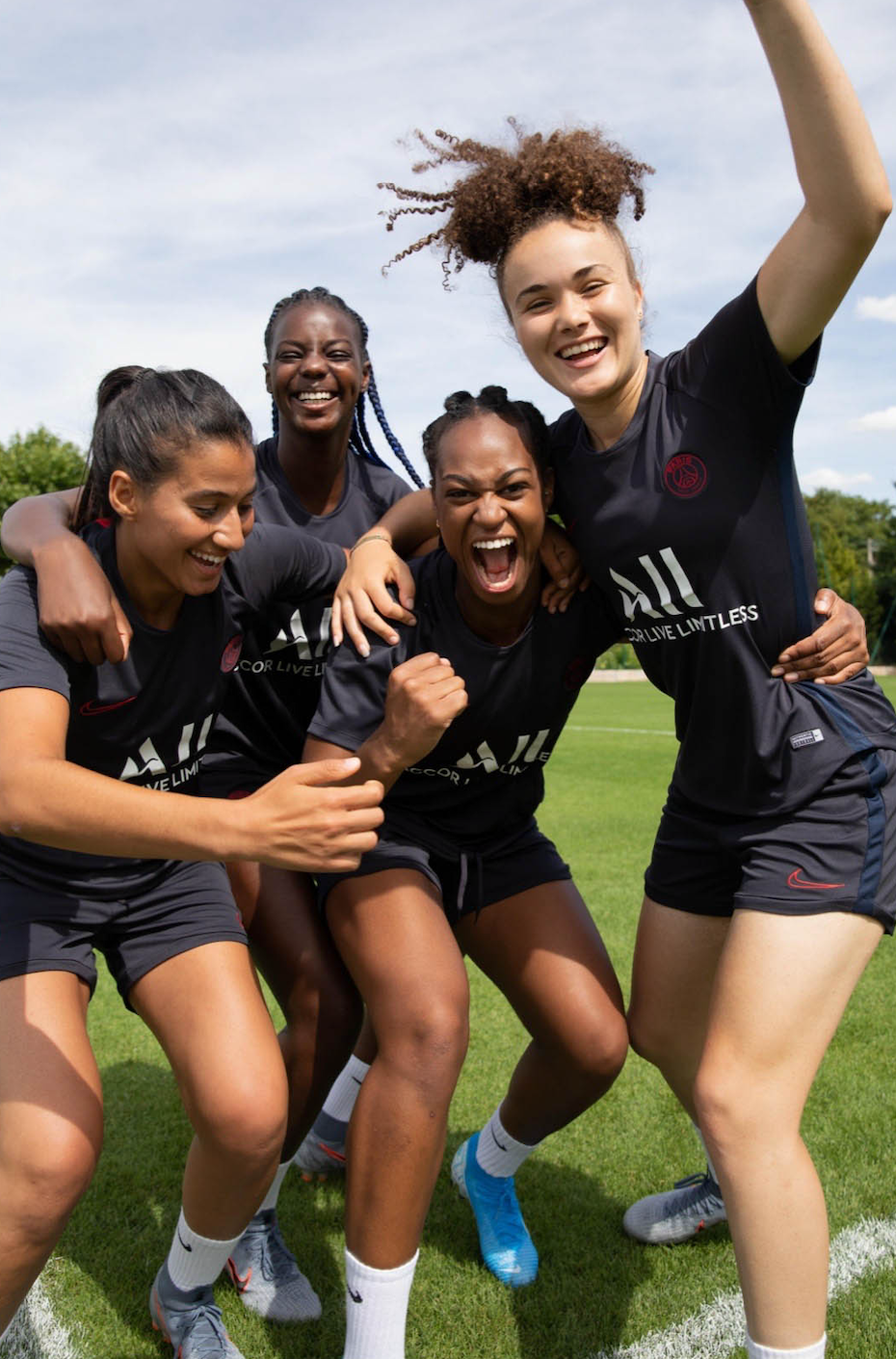 Group of four women soccer players celebrating on the field, smiling and showing excitement.