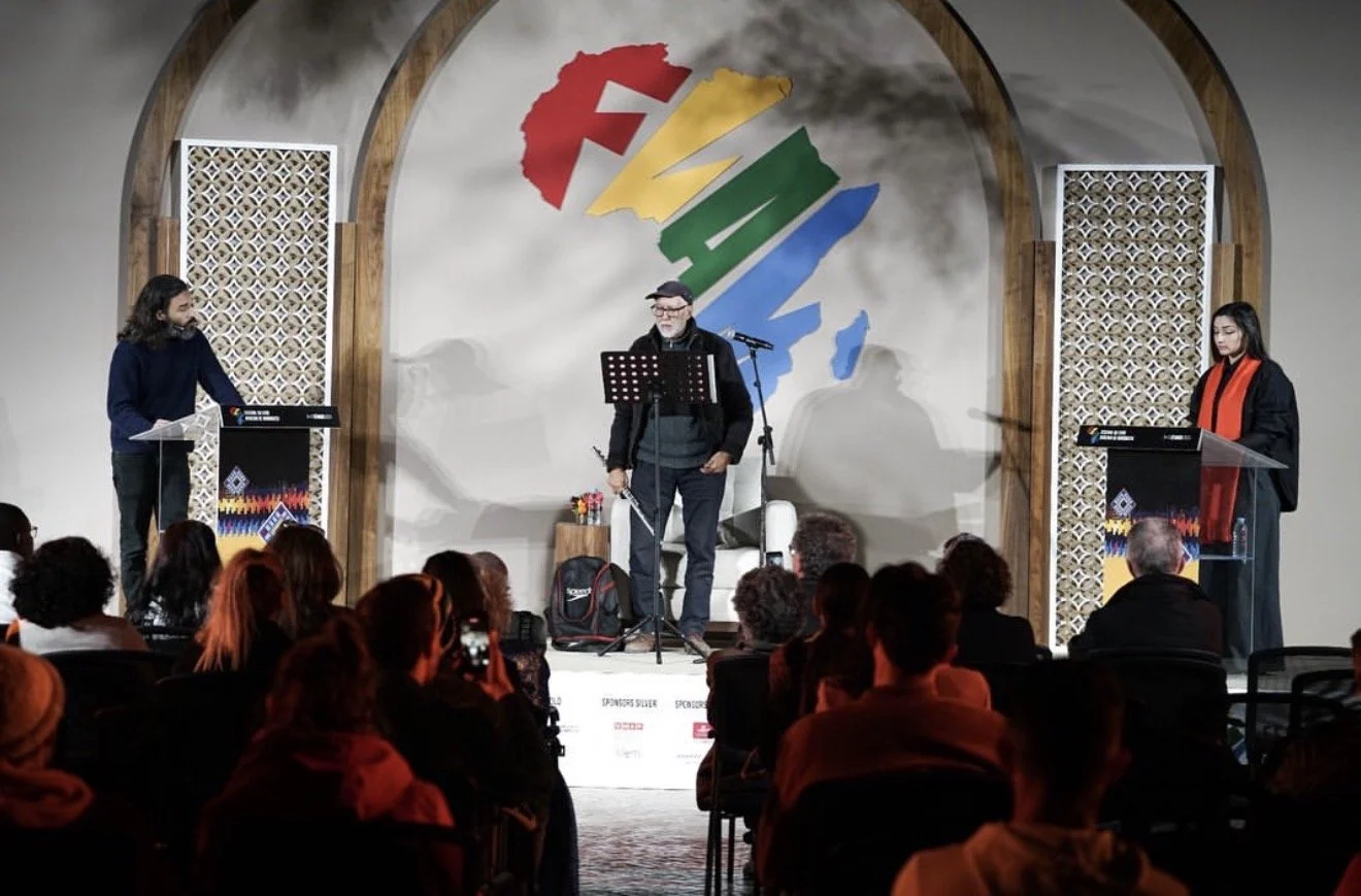 A stage with three speakers, two women and one man, addressing an audience at a cultural event. The backdrop features a large, colorful map of Taiwan with text in Chinese and English, and decorative panels on either side.