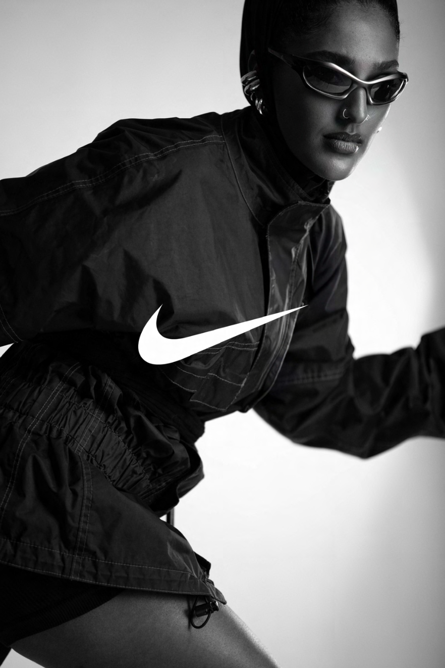 A black and white photo of a woman wearing sunglasses, a Nike logo on her jacket, and athletic clothing.