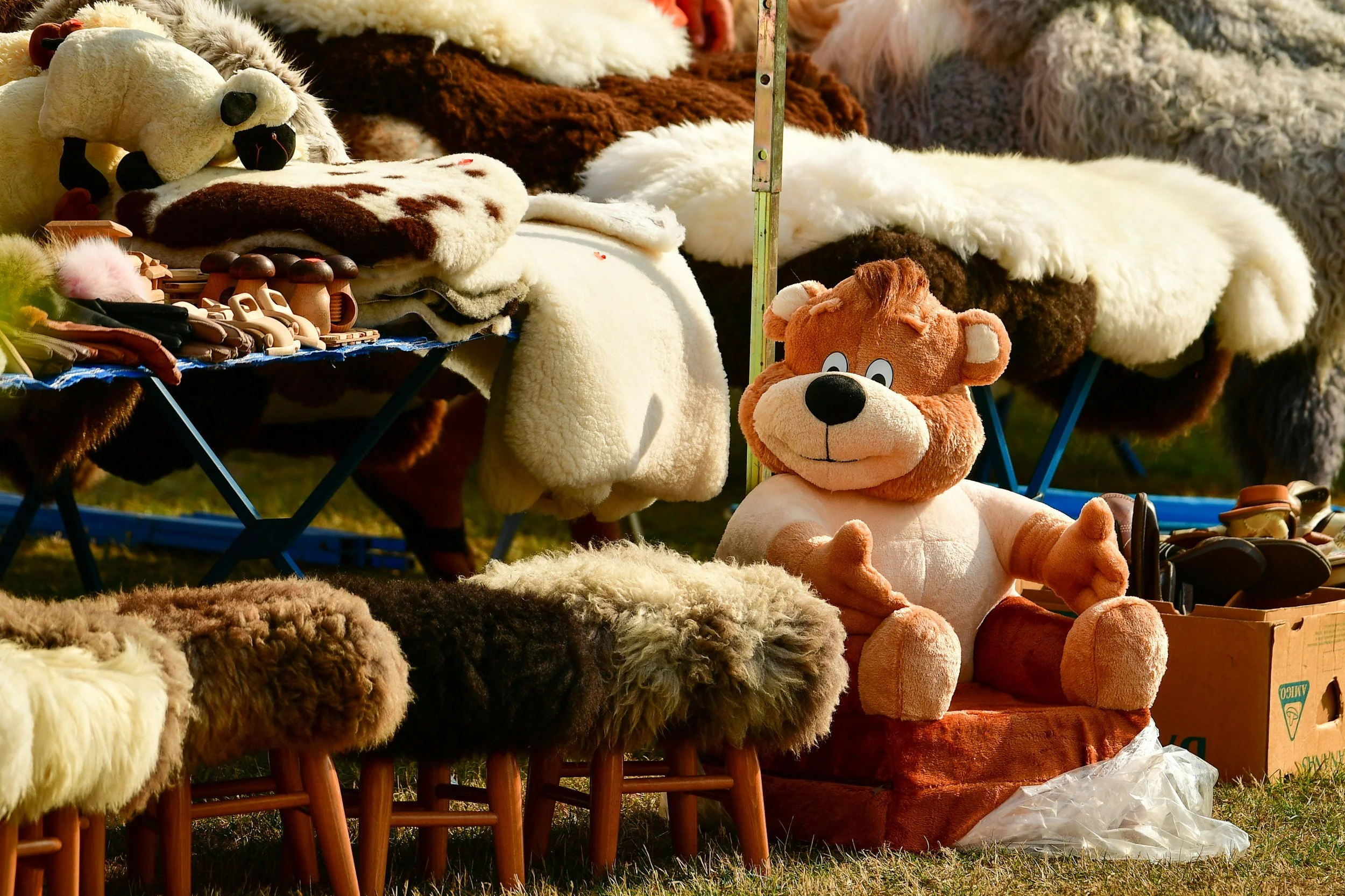 A variety of stuffed animal toys and plush blankets displayed on tables at an outdoor market.
