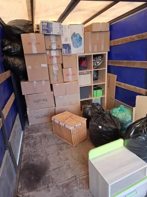 The image shows the interior of a moving truck filled with boxes, bags, and storage containers, with some open shelves and items inside.