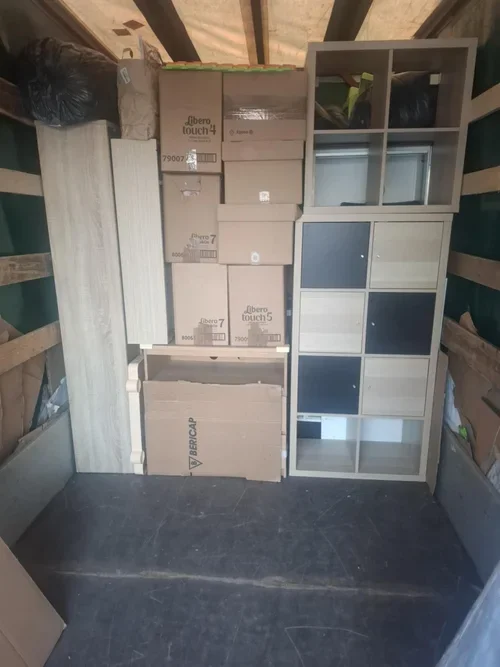 Stacked boxes and furniture inside a storage unit or warehouse, including cardboard boxes labeled 'Albero touch 4' and 'Albero touch 5,' and a glass-front cabinet.