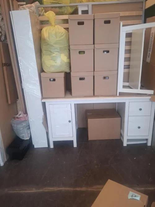 Various storage boxes and a white desk with drawers in a room, with a large yellow bag on top of the boxes.