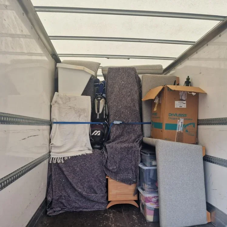 Interior of a moving truck loaded with furniture and boxes, secured with a blue strap.