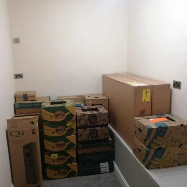 Empty room with stacked cardboard boxes on the floor, some with bananas and other designs, and a large sealed box on a raised platform.
