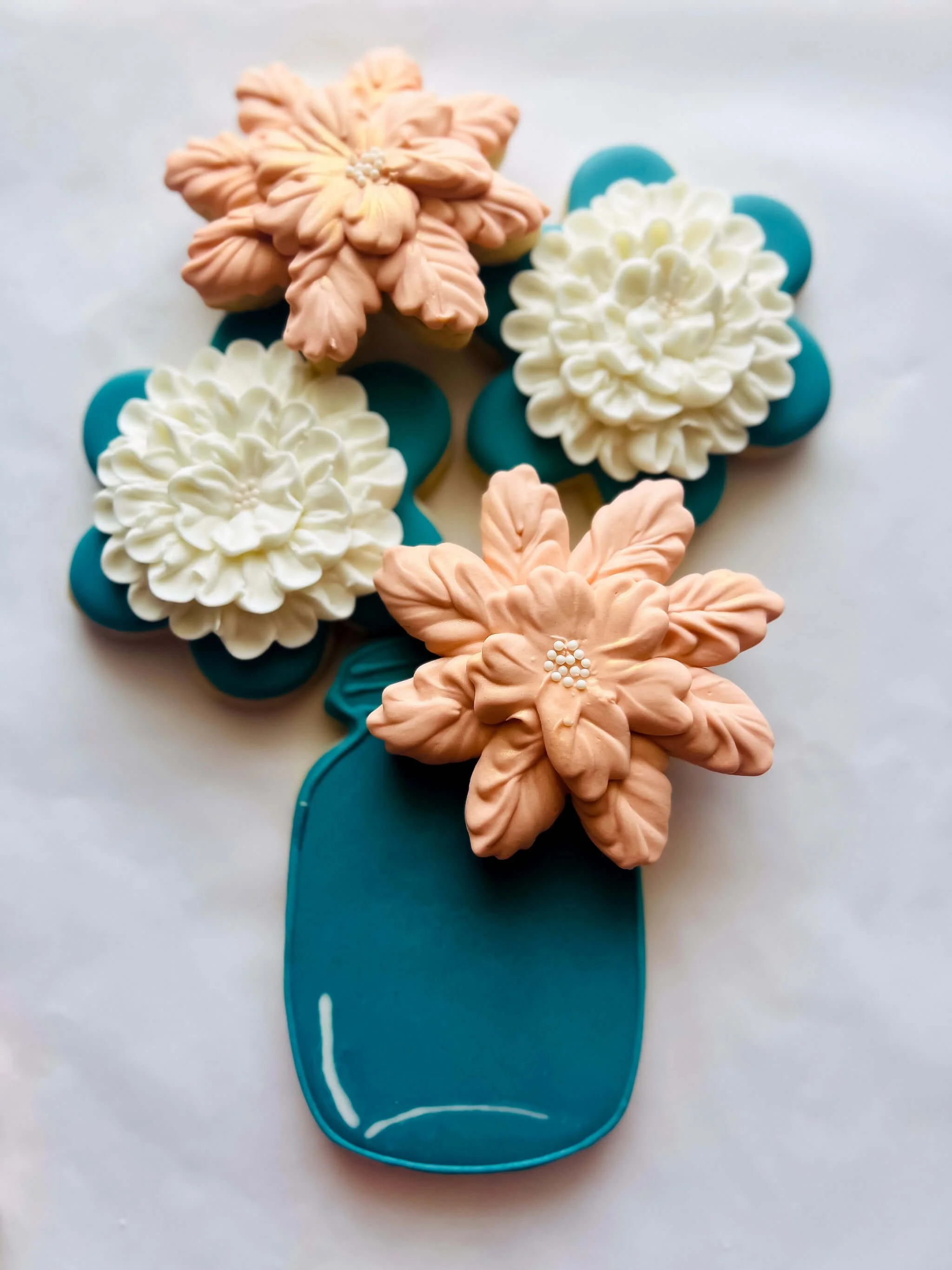 Decorative cookies in the shape of flowers arranged in a blue vase on a white surface.