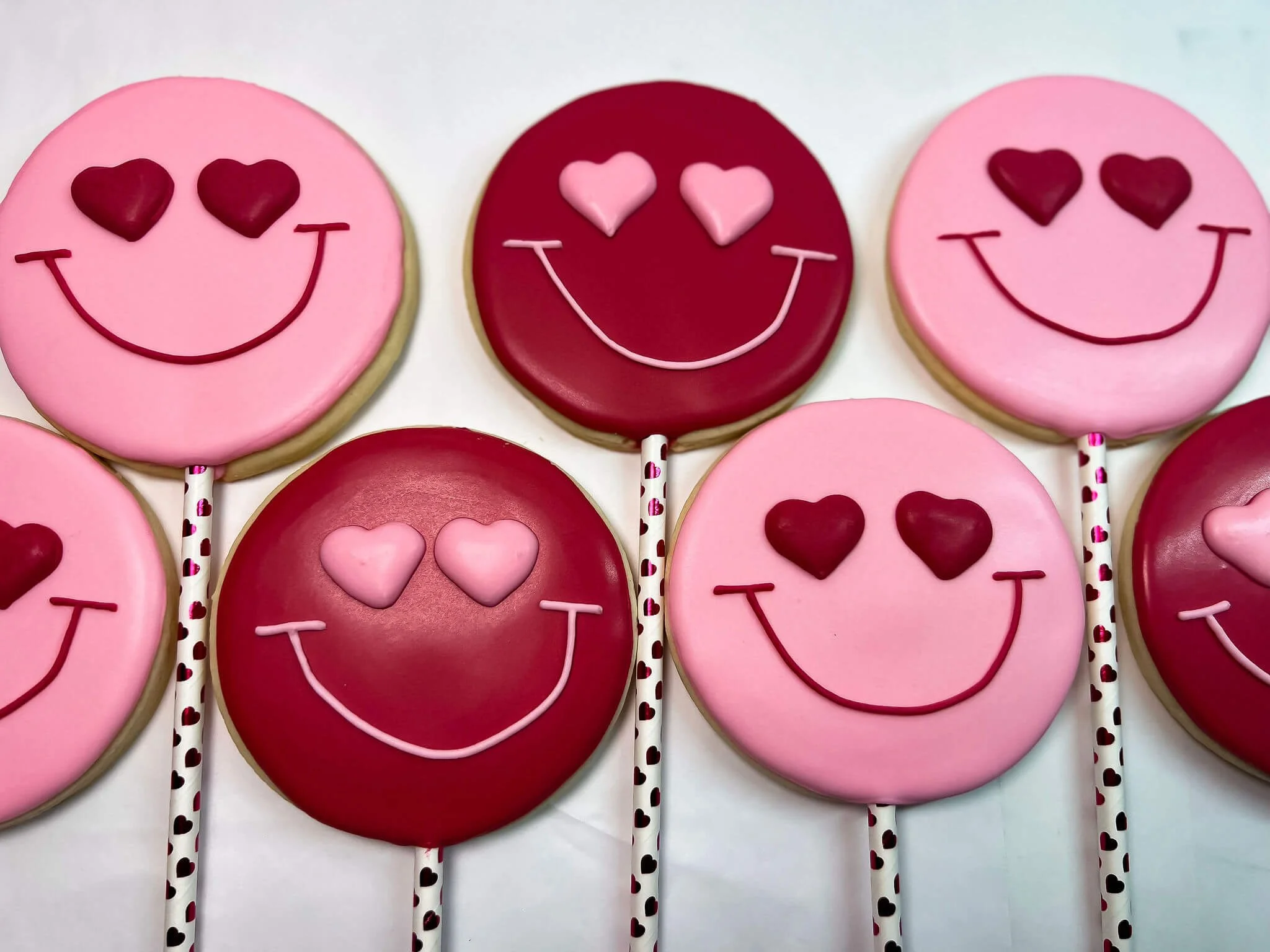 Decorated lollipops with smiley faces and heart-shaped eyes, in pink and red colors.