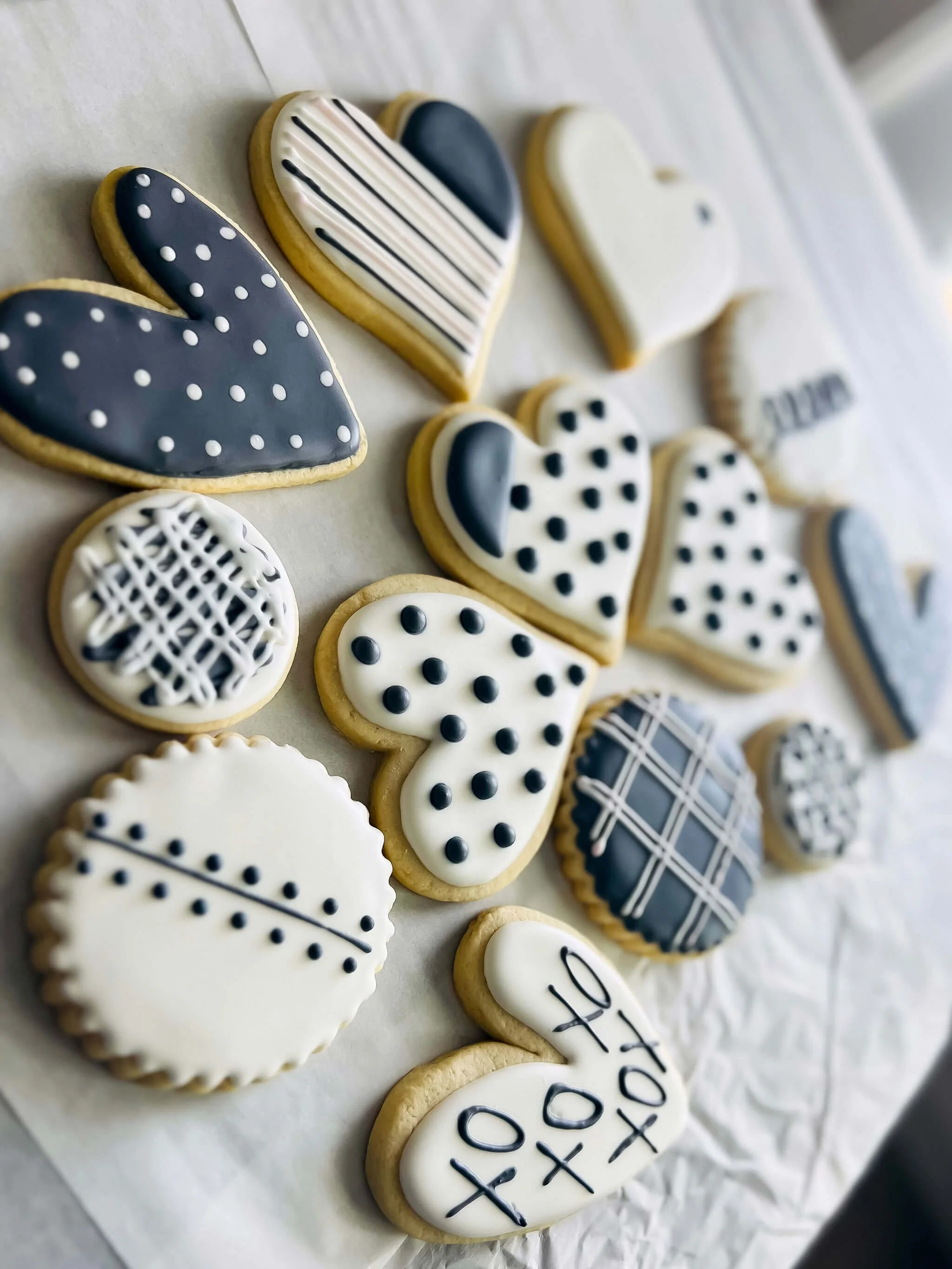 Decorated cookies in black, white, and gray with various patterns including polka dots, stripes, plaid, and cross-hatches, arranged on a white sheet.