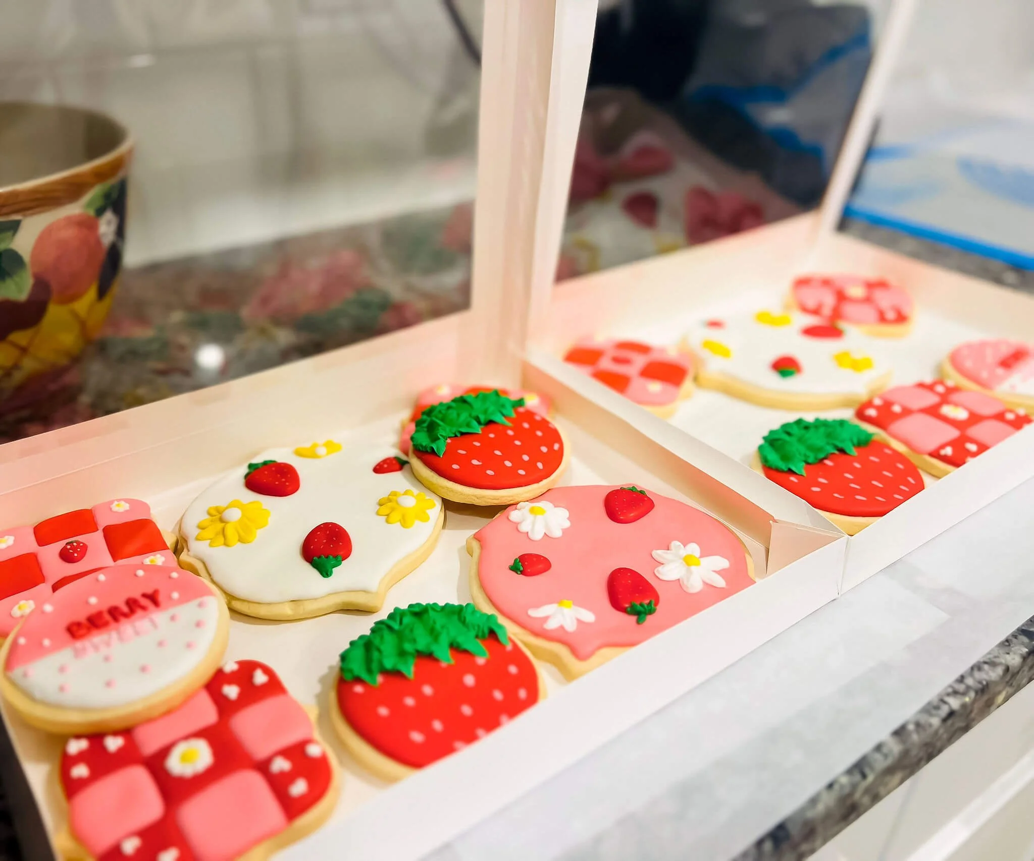 Assorted decorated cookies on a white tray, featuring strawberries, flowers, and strawberries with text that reads 'berry' and 'happy.'