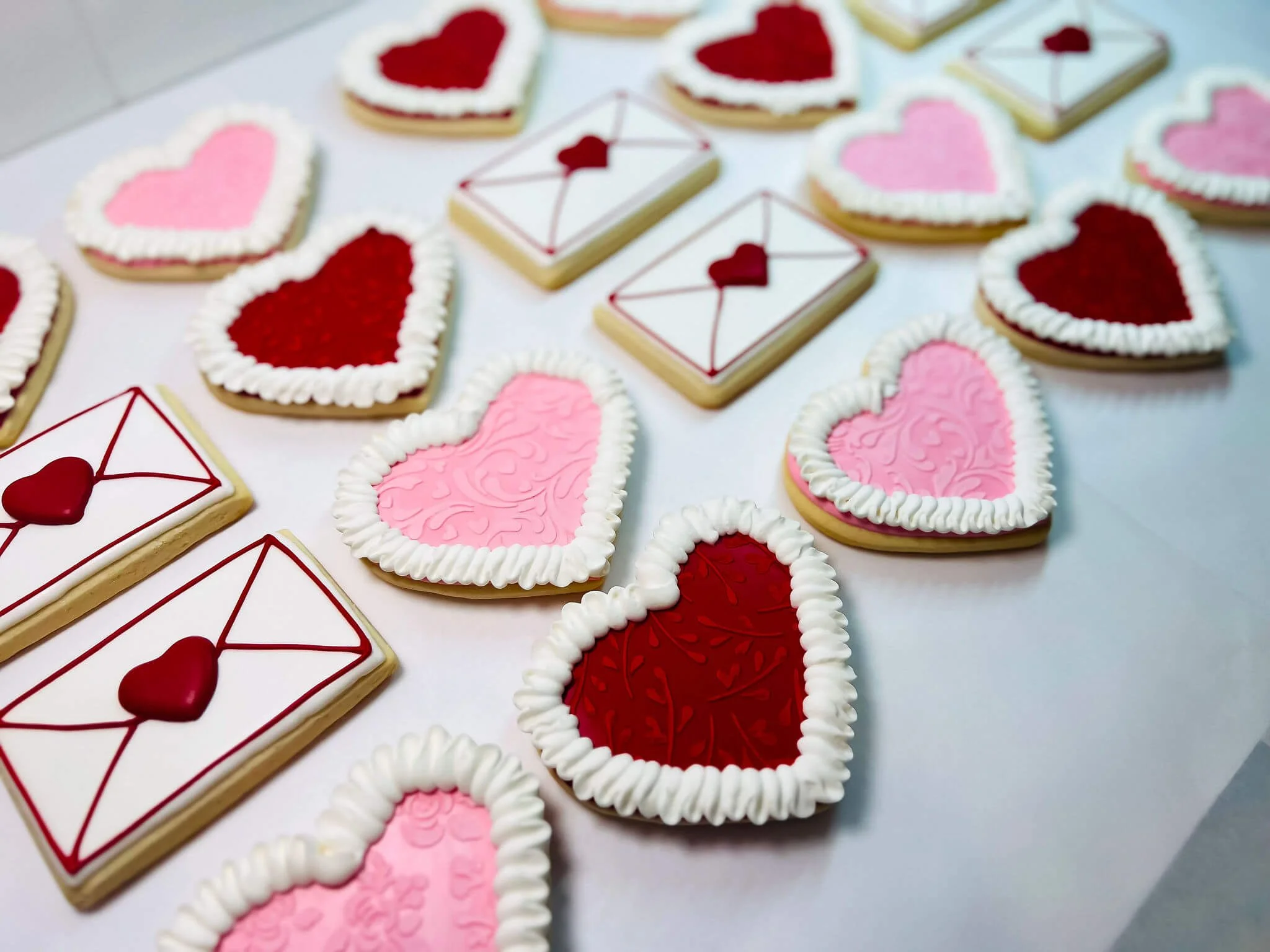 Decorated heart and envelope-shaped cookies with red and pink icing, arranged on a white surface.