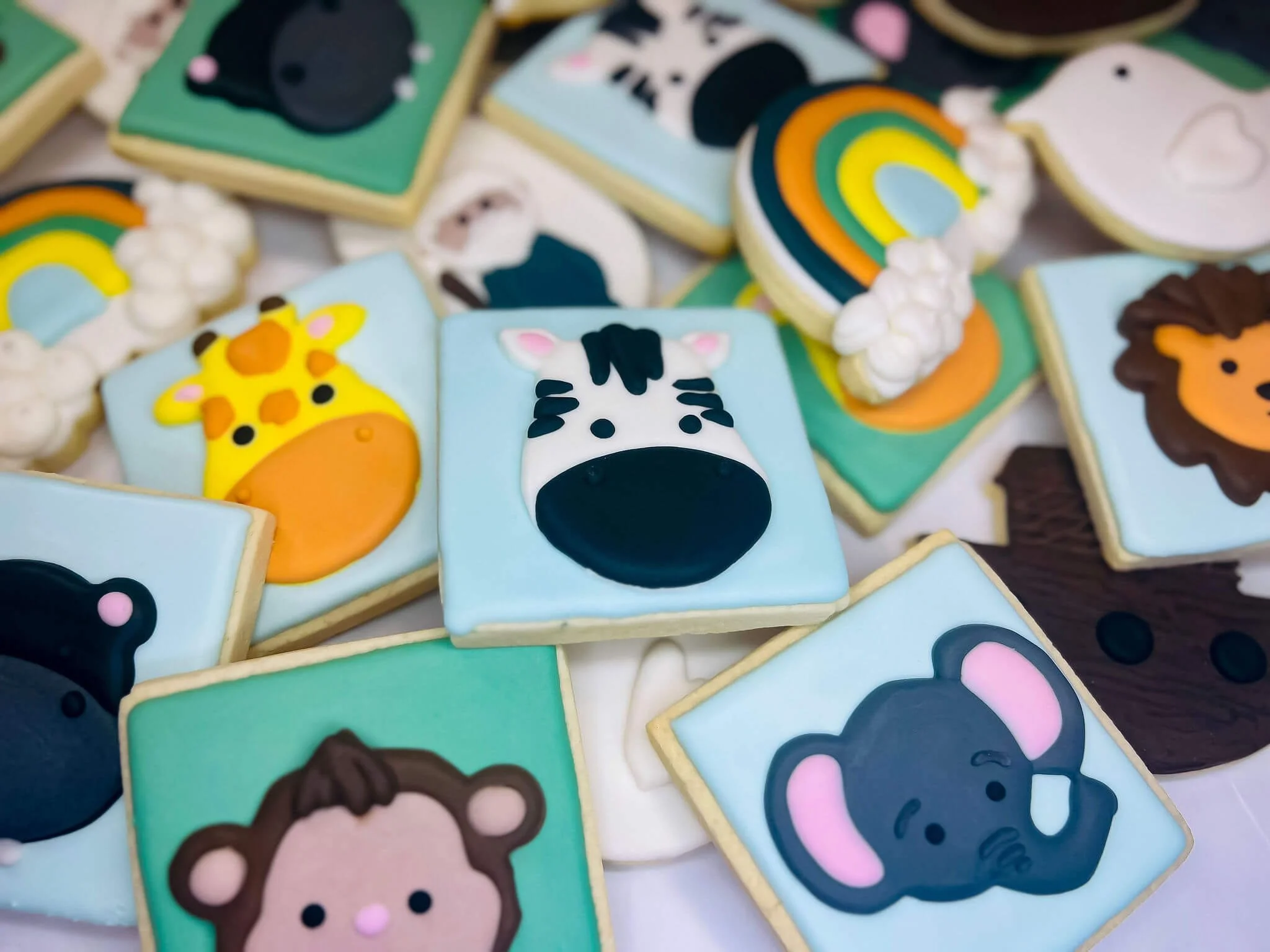 Colorful animal themed sugar cookies decorated with icing, featuring a giraffe, zebra, lion, koala, elephant, and monkey, among other animal designs.