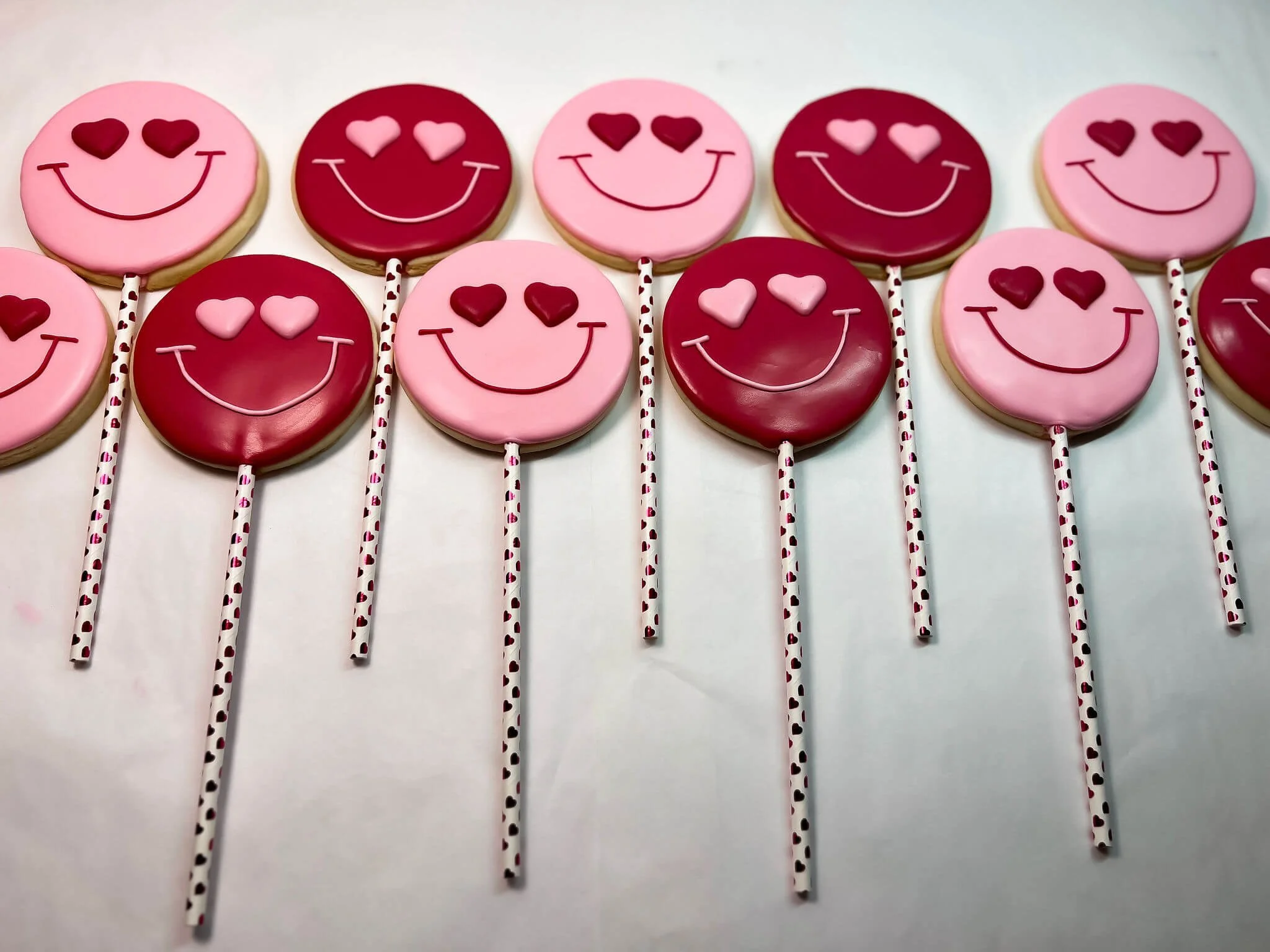 Decorative lollipops with smiley faces and heart-shaped eyes in pink and red colors, arranged on a white surface.