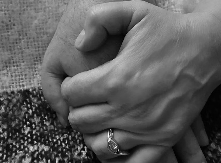 Close-up of two hands clasped together on a textured surface, with a ring on the finger.