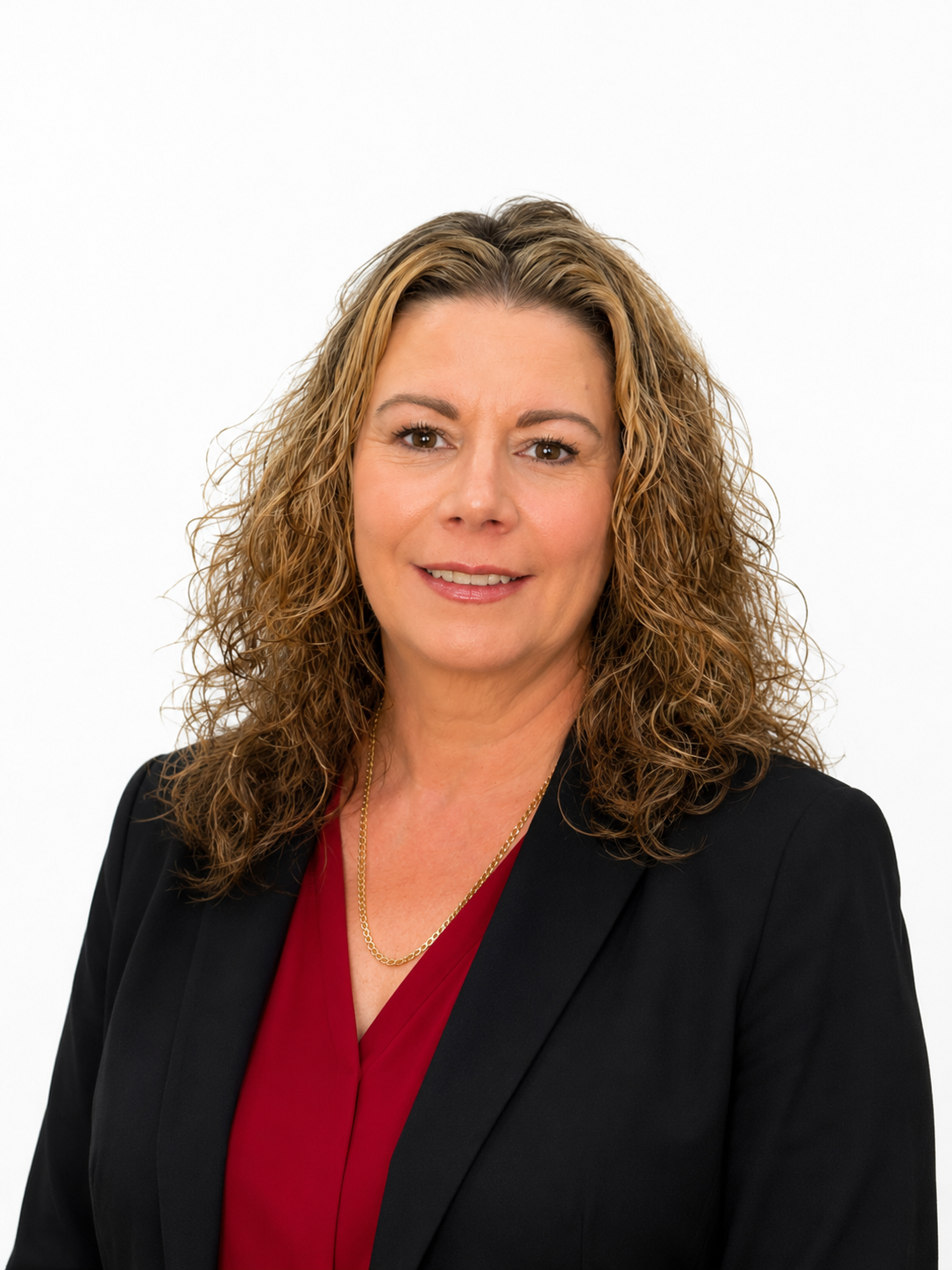 Headshot of a woman with curly brown hair, wearing a black blazer and a red top, smiling against a plain white background.