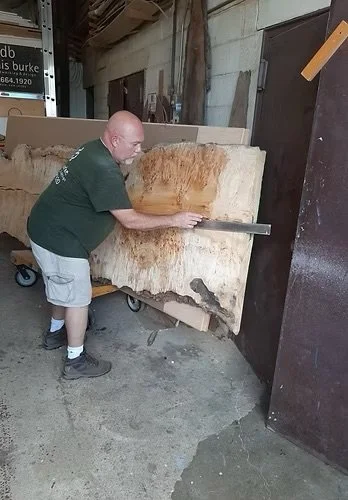A man using a handsaw to cut a large piece of wood in a workshop or warehouse.