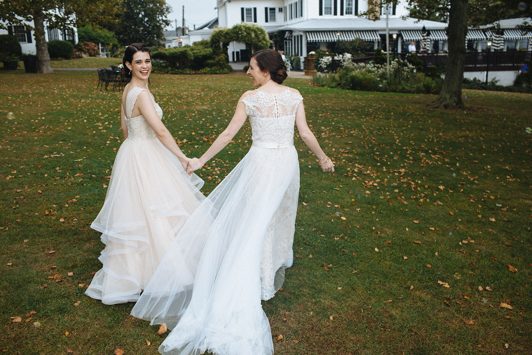 Lauries Kundinnen Mariana und Carmen halten an ihrem Hochzeitstag auf einer grünen Wiese Händchen.