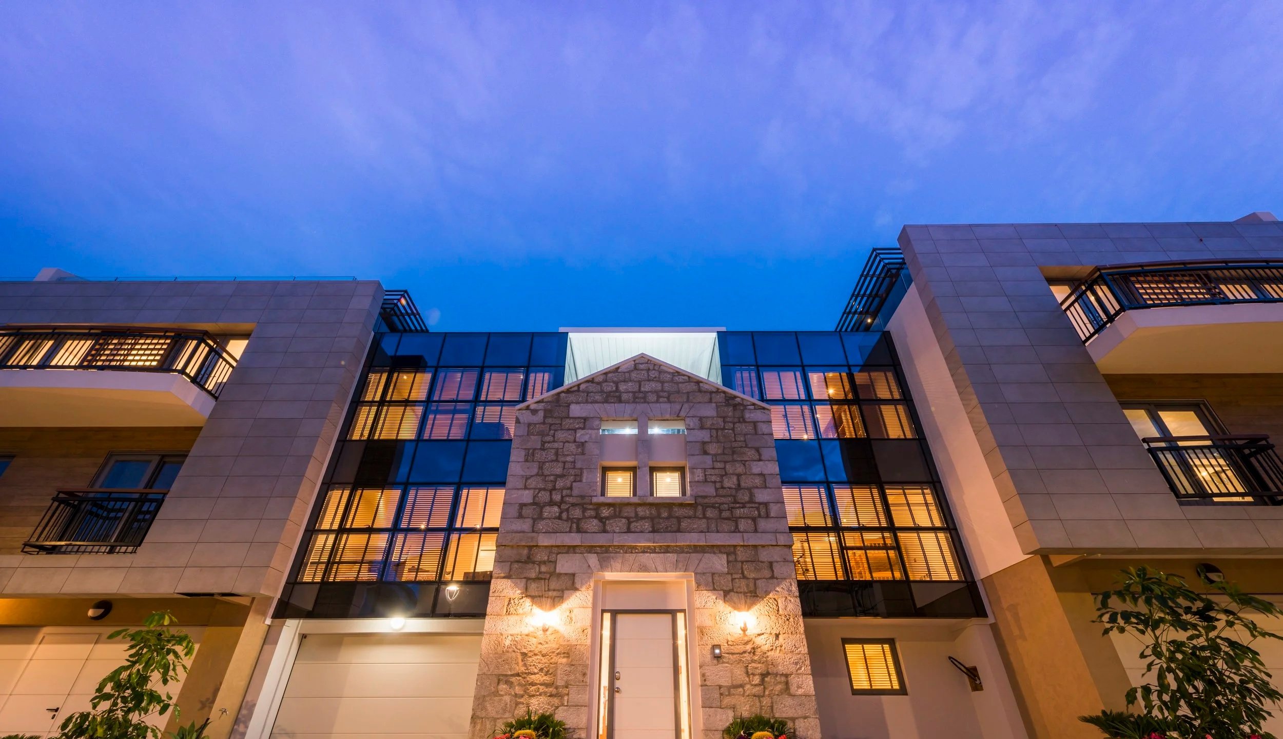 Modern residential building at dusk with lit windows and a stone entrance, under a blue evening sky.