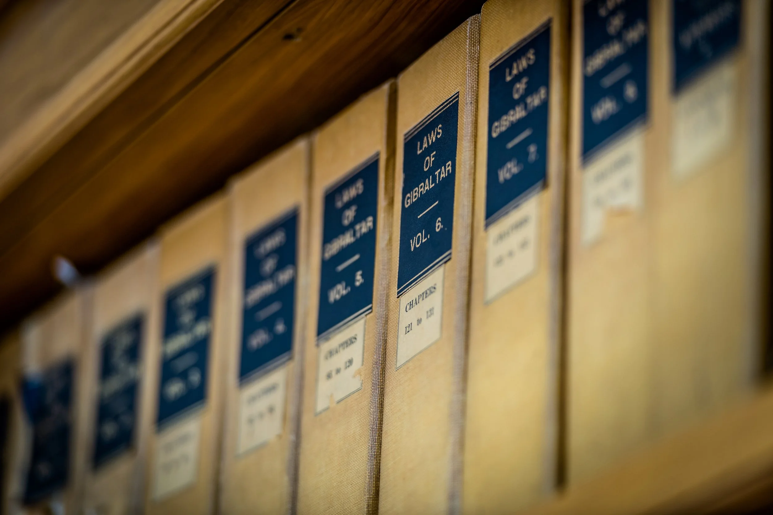 A row of books titled 'Laws of Gibraltar' on a wooden bookshelf.