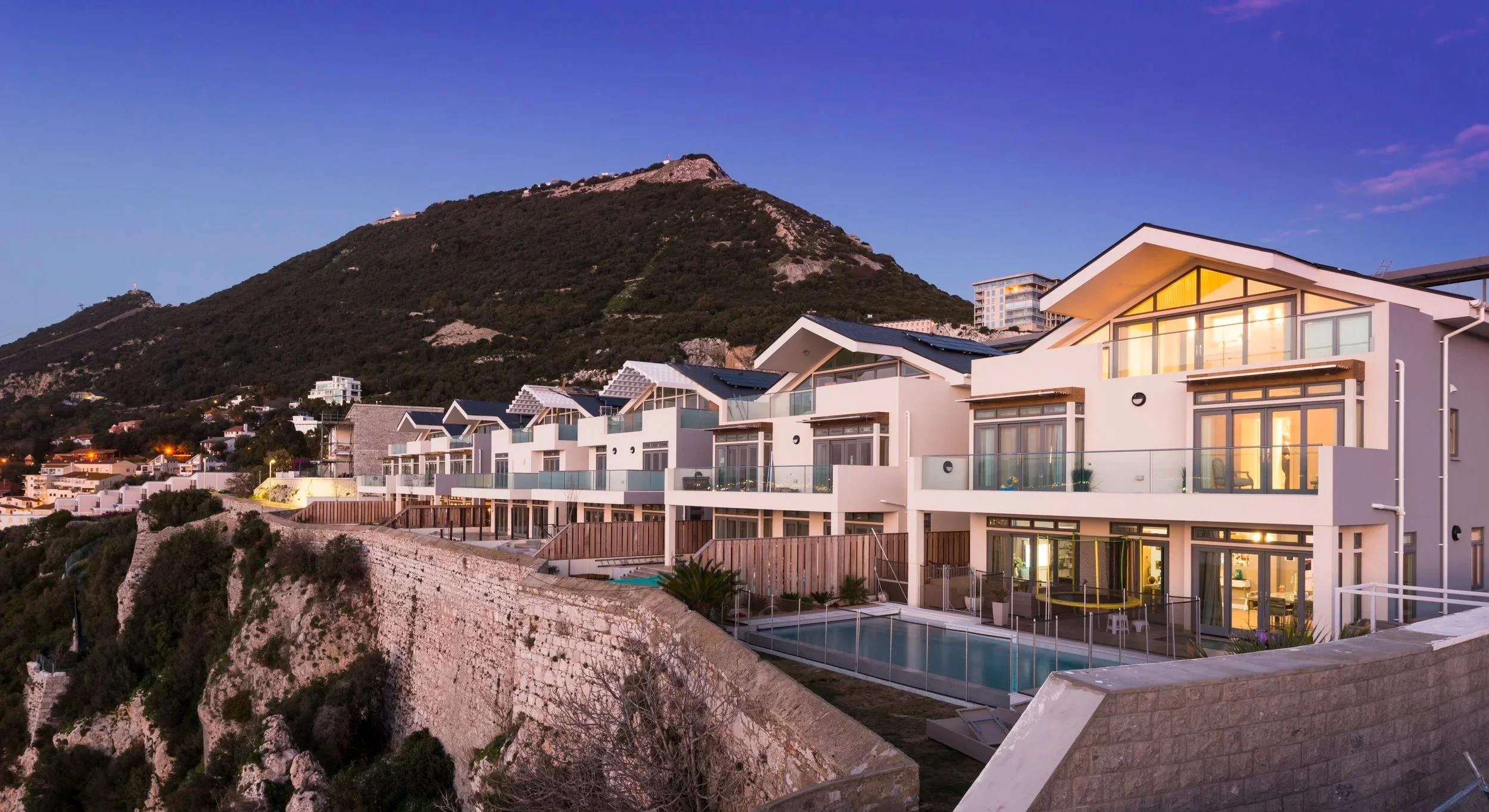Modern white residential buildings on a hillside with a mountain in the background during dusk.