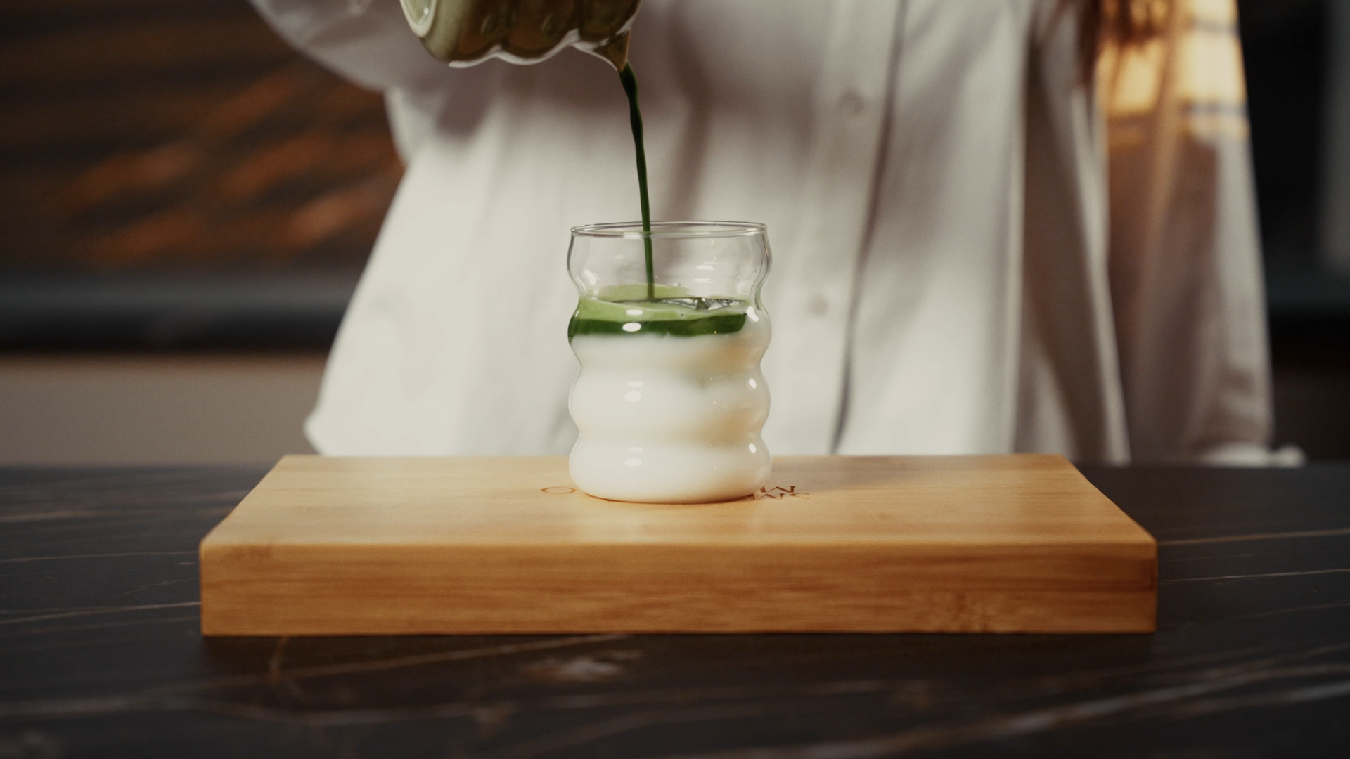 Een glas met matcha op een houten plank op een donkere tafel.