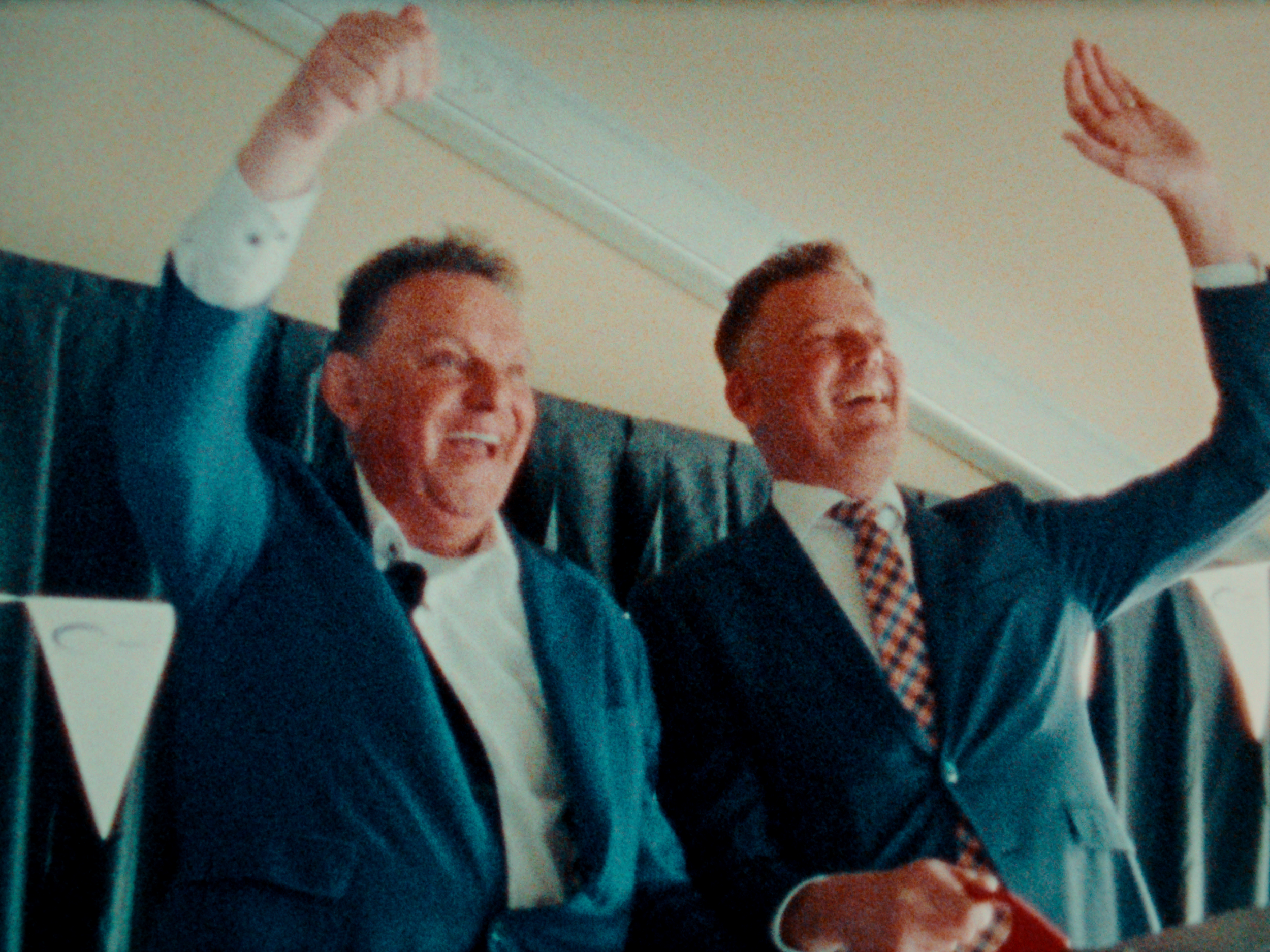 Twee mannen lachen en vinken terwijl ze in een kantoor of vergaderruimte zitten.