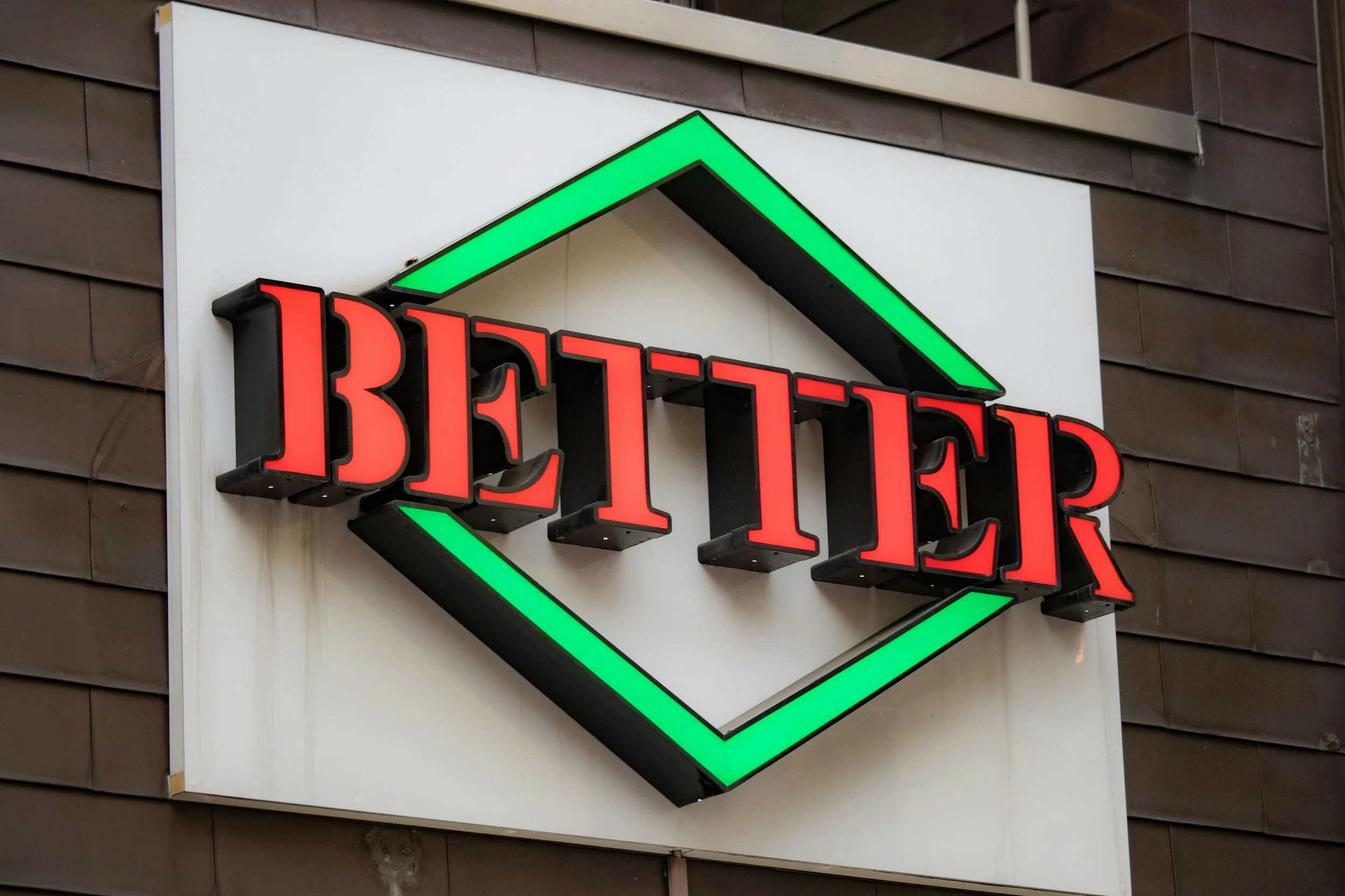 Neon sign with the word 'BEER' in red letters inside a diamond-shaped outline with green borders, mounted on a building's exterior wall.