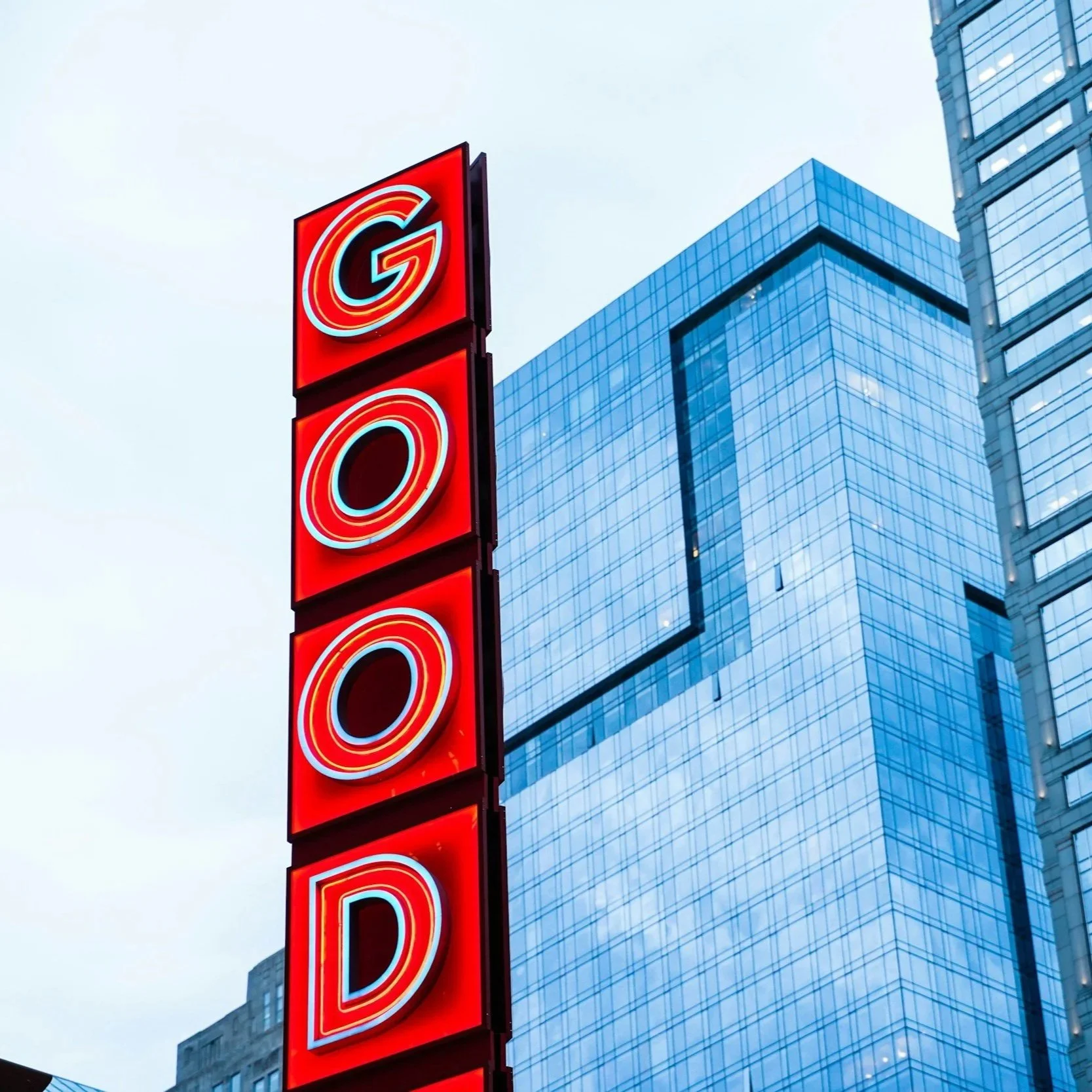 A tall neon sign spelling "GOLD" in red and blue letters against a modern glass building in a city.