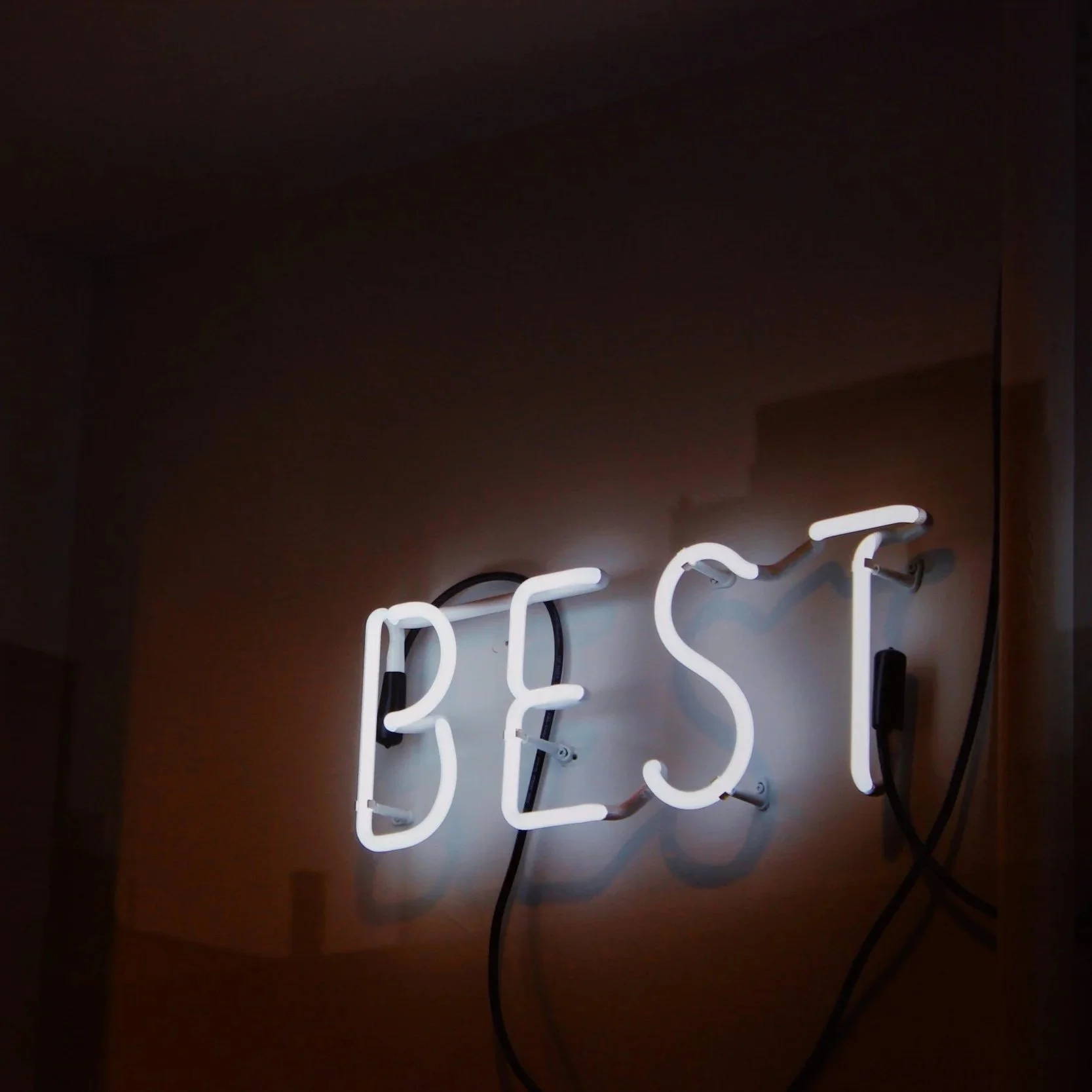 Illuminated white neon sign spelling 'BEST' mounted on a beige wall.