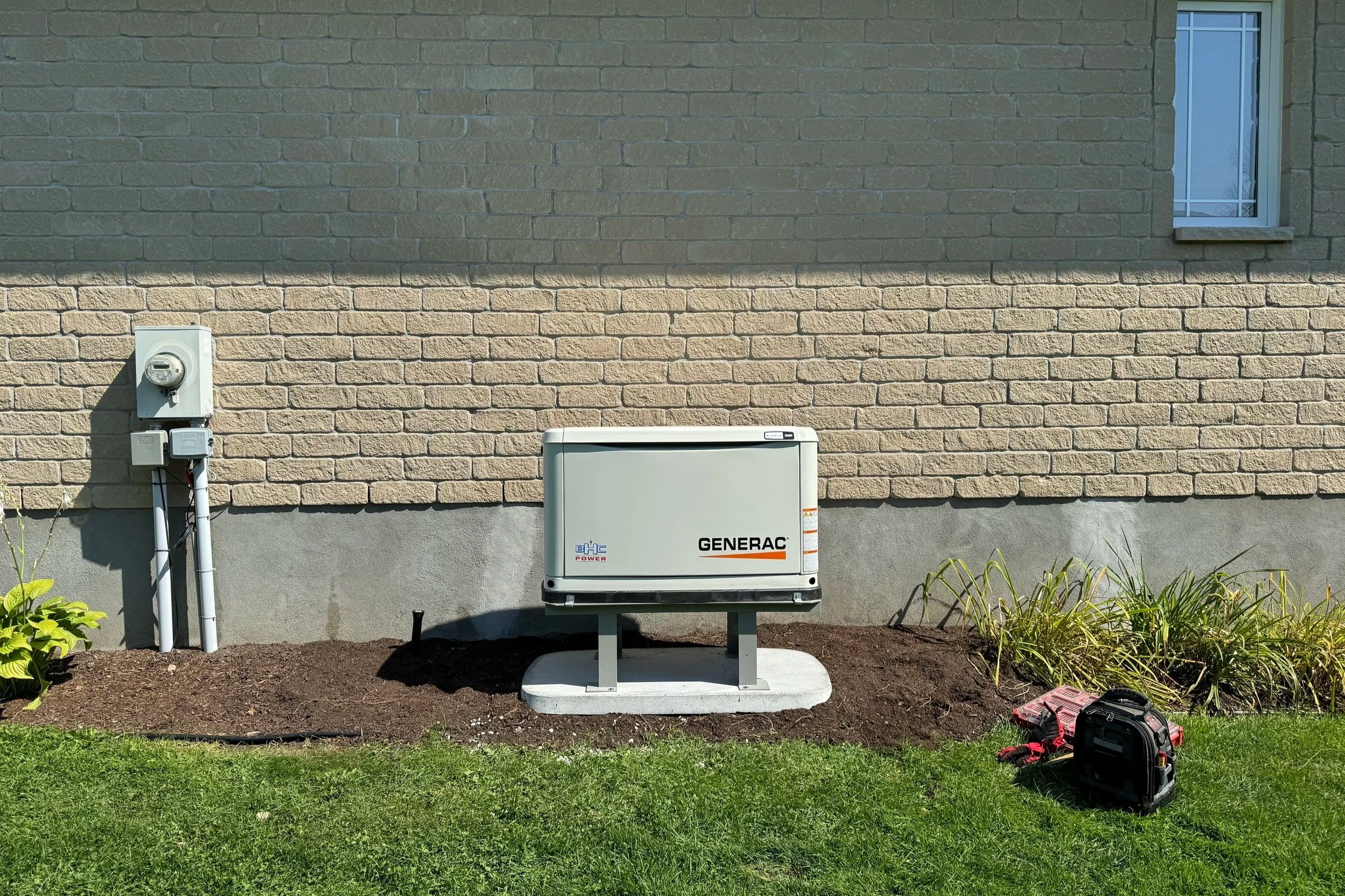 Exterior of a house with a Generac generator outside, electrical meter on the wall, and some tools on the ground.