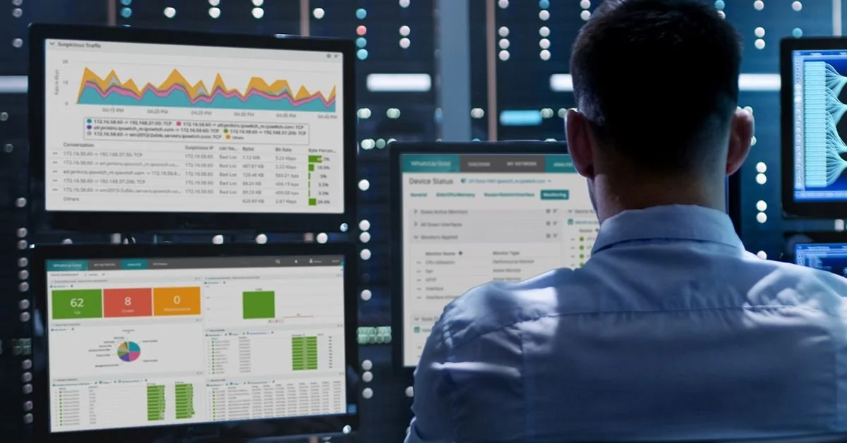 A man sitting at a desk monitoring multiple screens displaying graphs, charts, and data analytics in a high-tech control room.