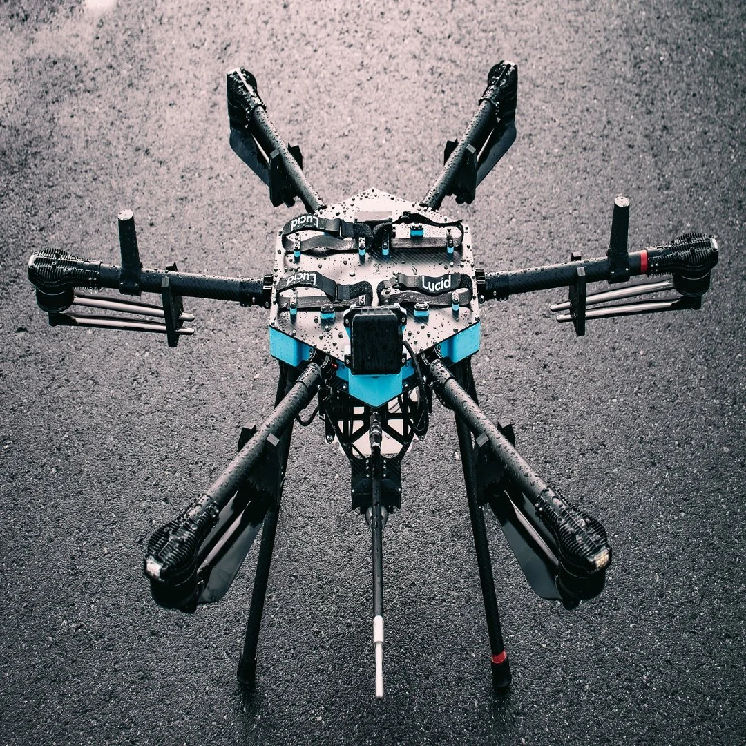 A drone with six arms and a central body, placed on asphalt ground, equipped with various components for stability and control.