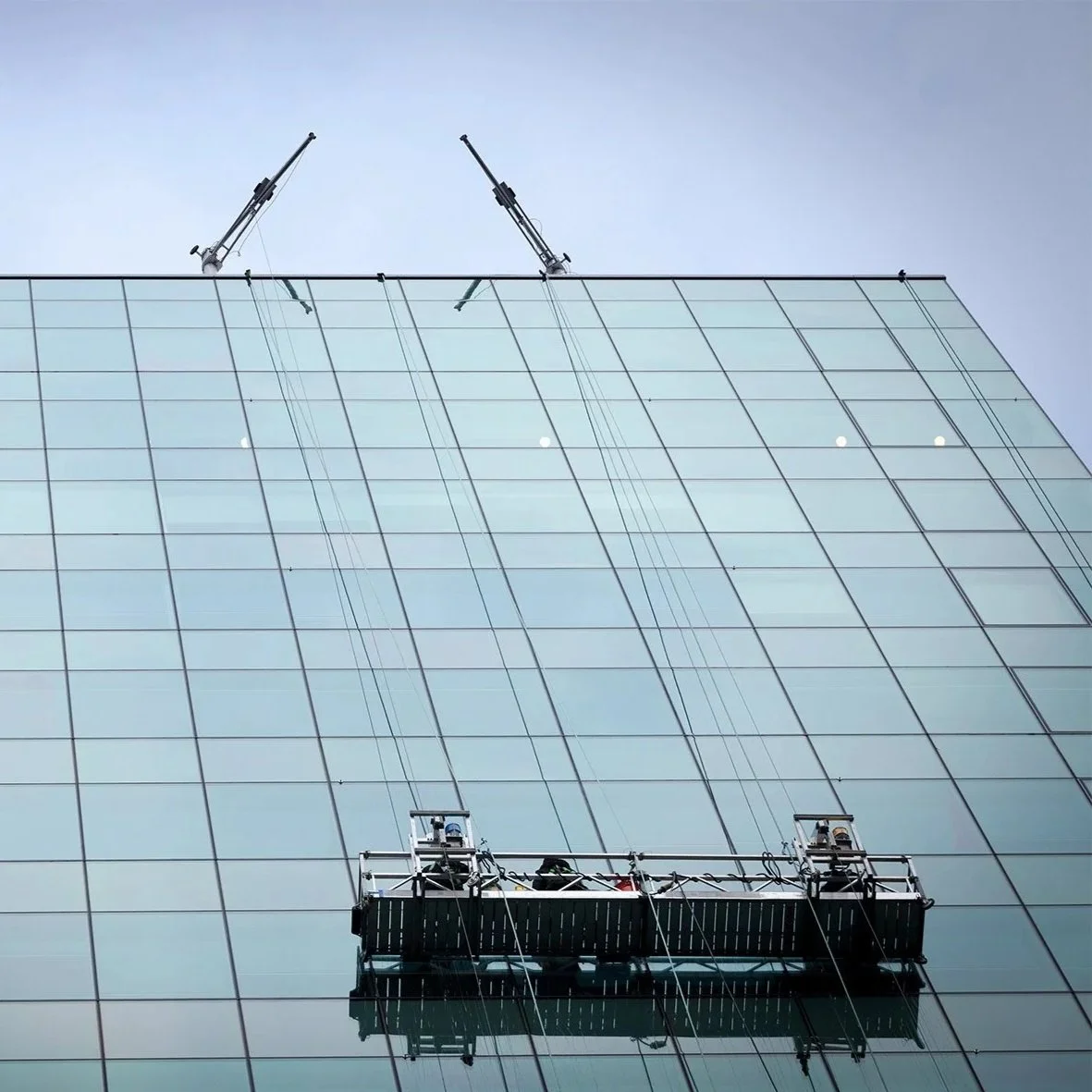 Cleaning crew power washing the glass exterior of a tall modern building with reflective windows.