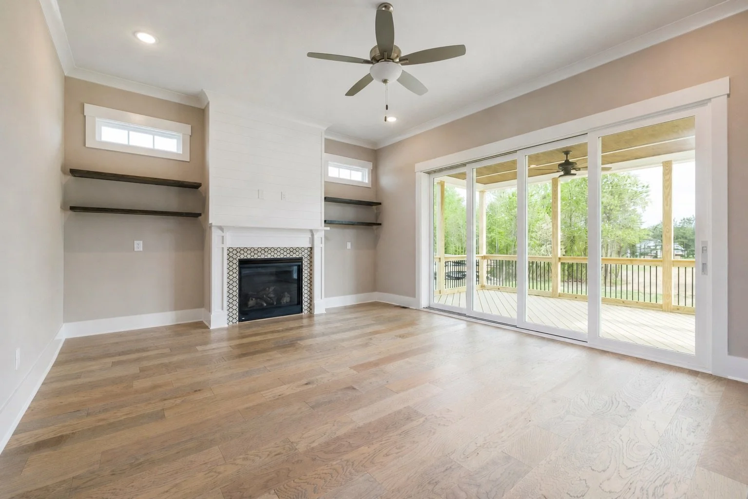 Empty living room with wooden floors, a fireplace, large sliding glass doors leading to a porch, and a ceiling fan.