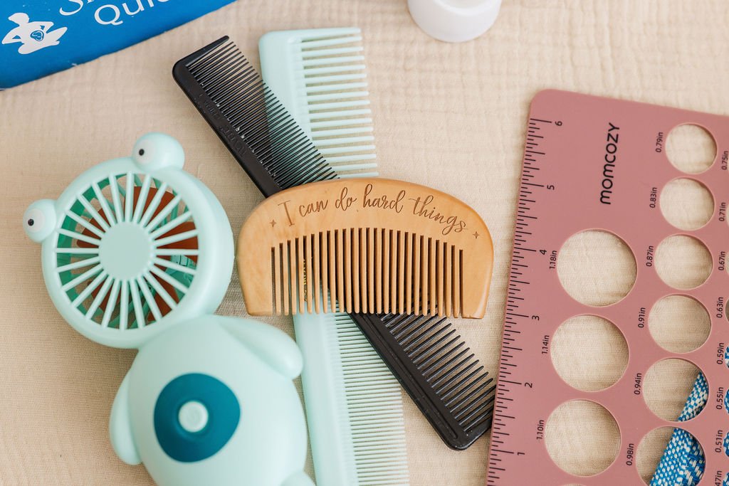 Collection of labor coping tools including combs, a pink nipple ruler, a small fan, and a wooden hair comb with the quote 'I can do hard things' written on it, all arranged on a light-colored surface.