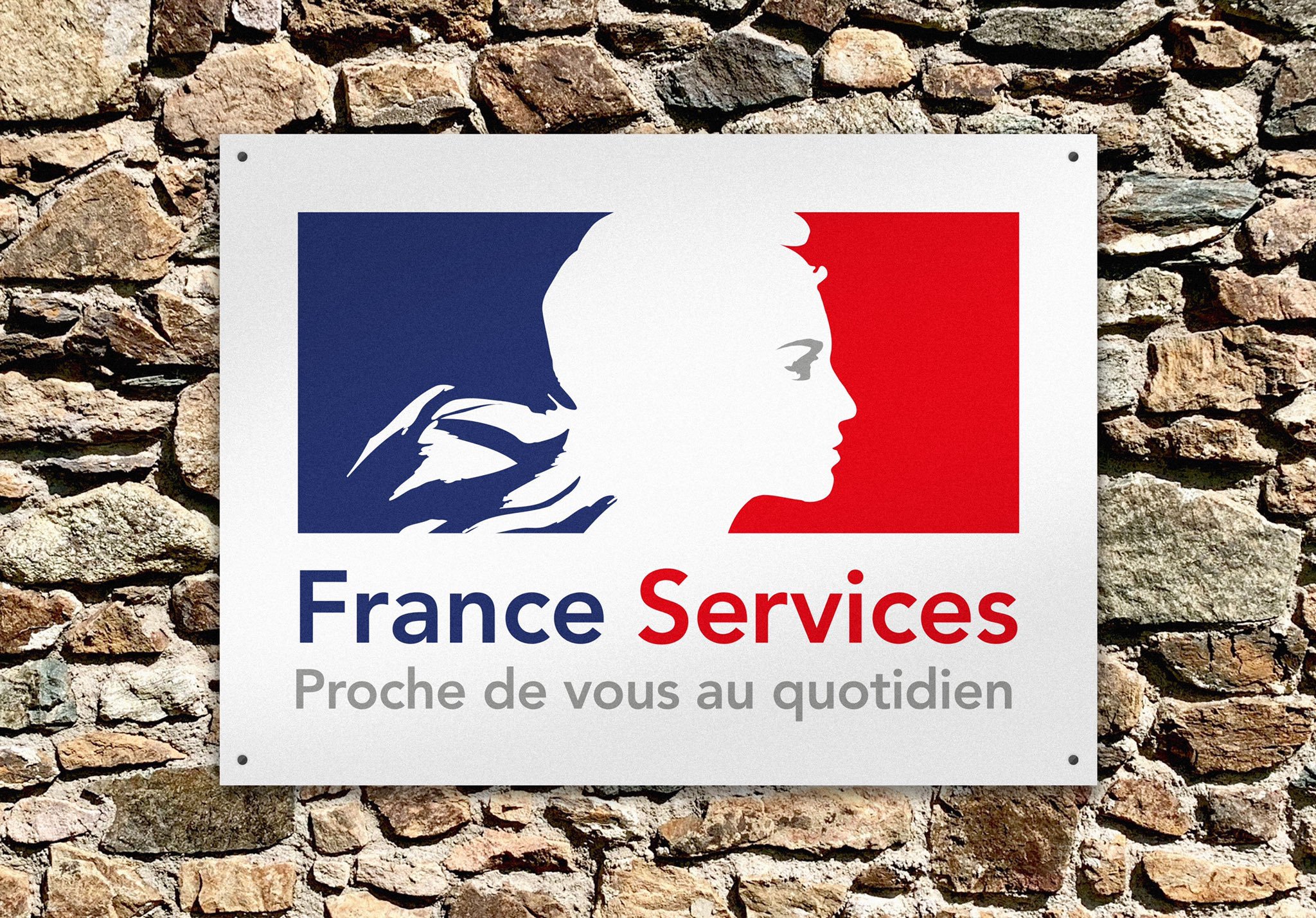 Panneau avec logo stylisé d'une tête de lion, couleurs bleu, blanc, rouge, texte "France Services" et slogan "Proche de vous au quotidien" devant un mur en pierre.