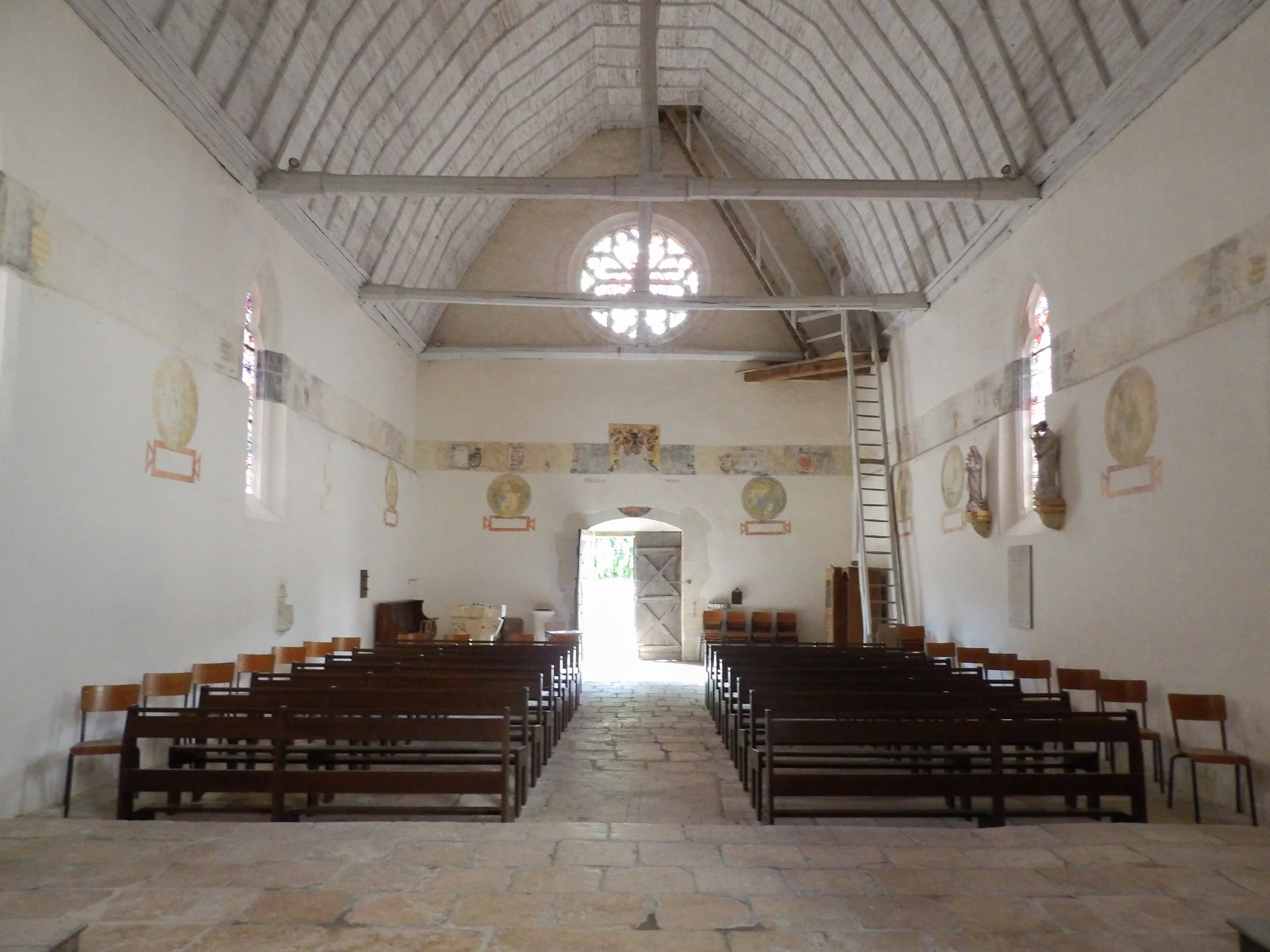 Intérieur d'une église avec deux rangées de chaises en bois, des vitraux colorés et une rosace au plafond.
