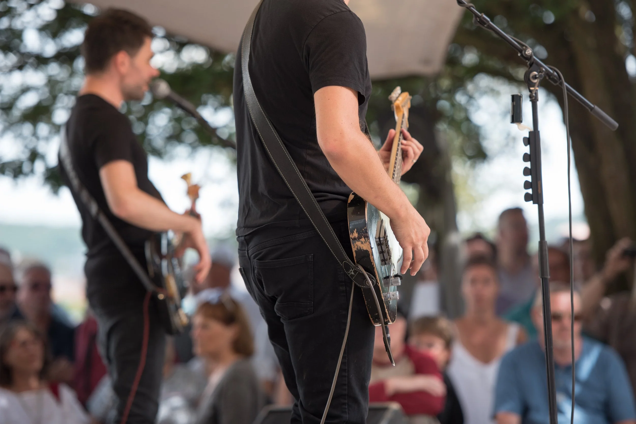 Musiciens jouant de la guitare lors d'une performance en extérieur, avec un public regardant.