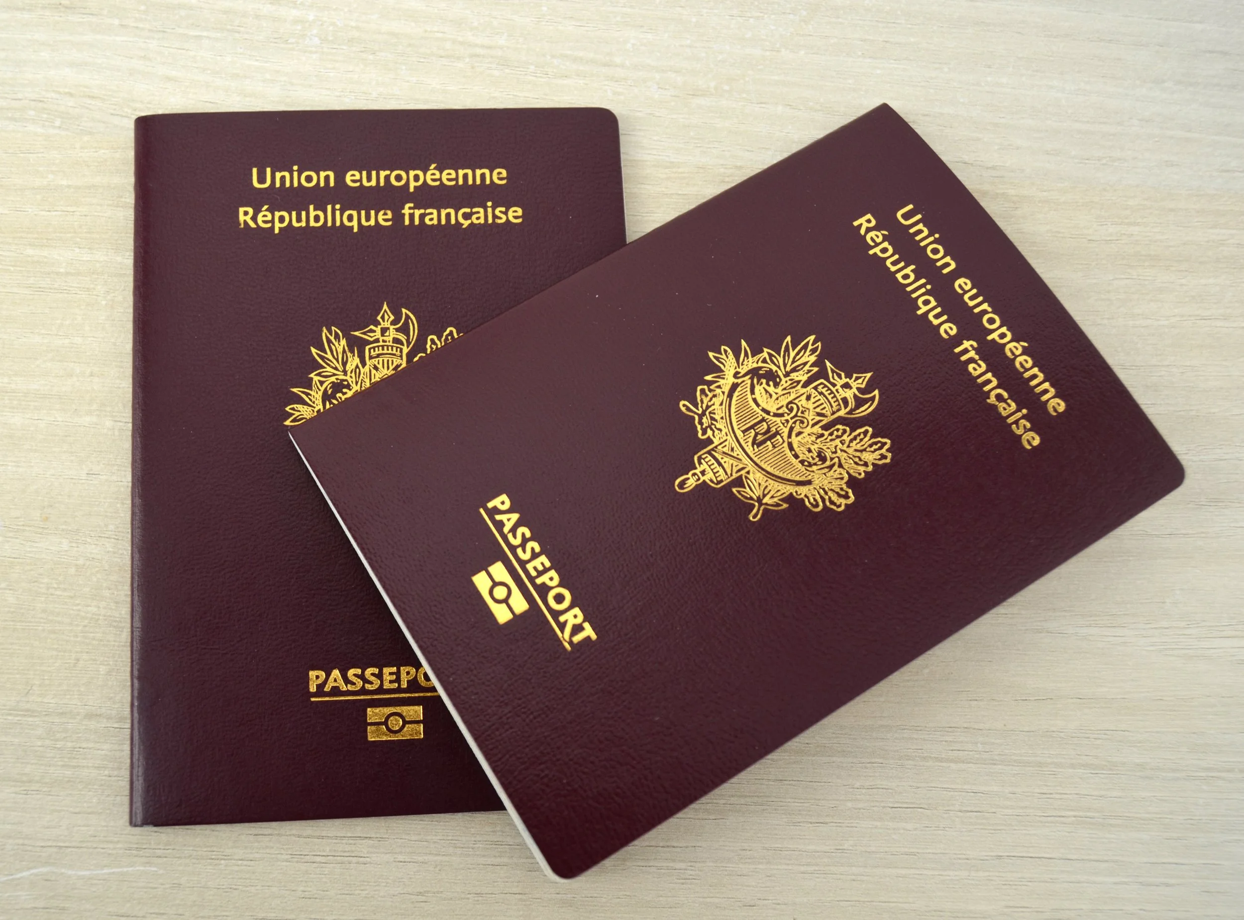 Deux passeports français de couleur bordeaux avec un blason doré et écrit en français, posés sur une surface en bois claire.